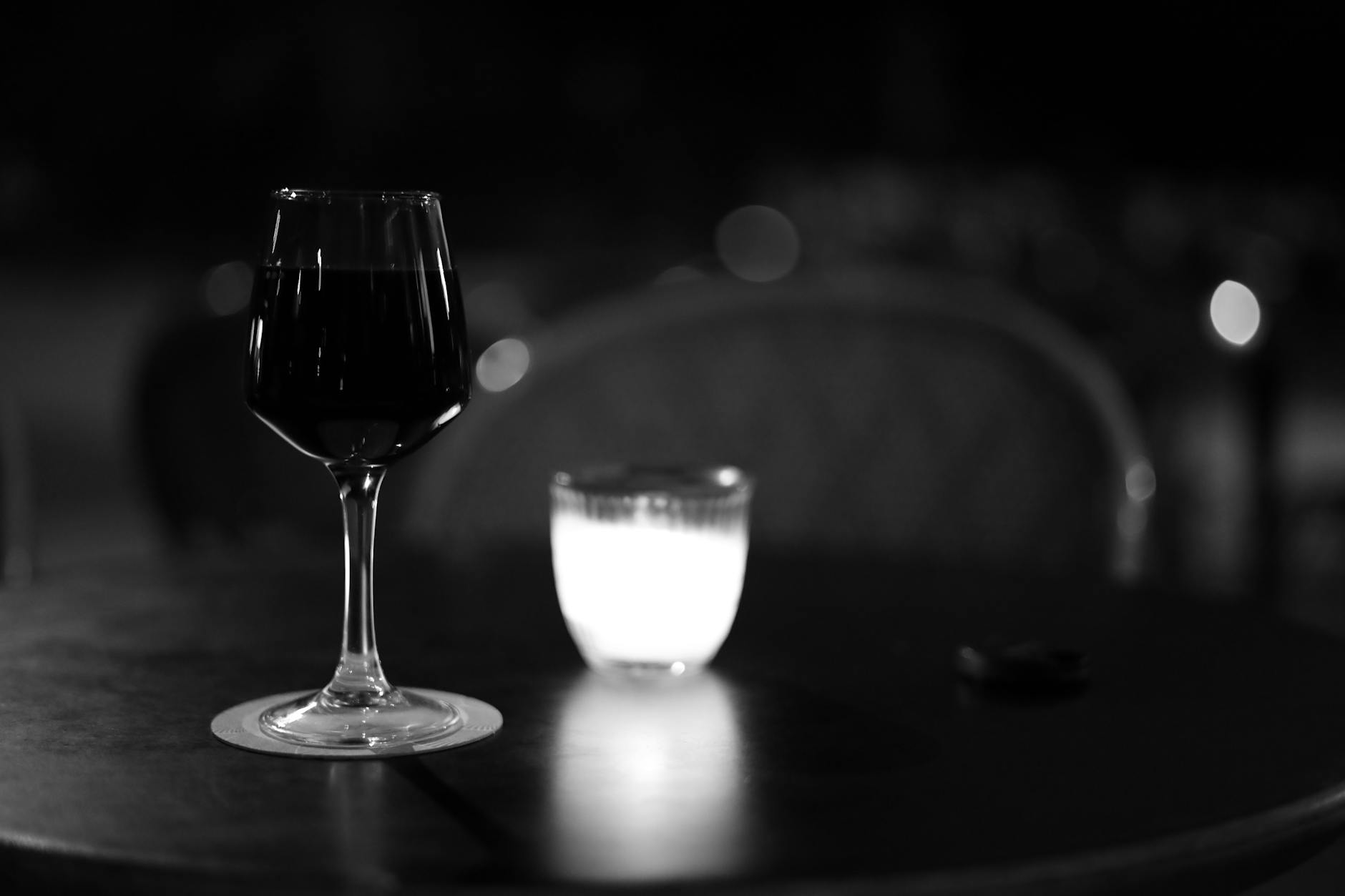 A glass of wine and a candle on a table in a Paris café setting at night.