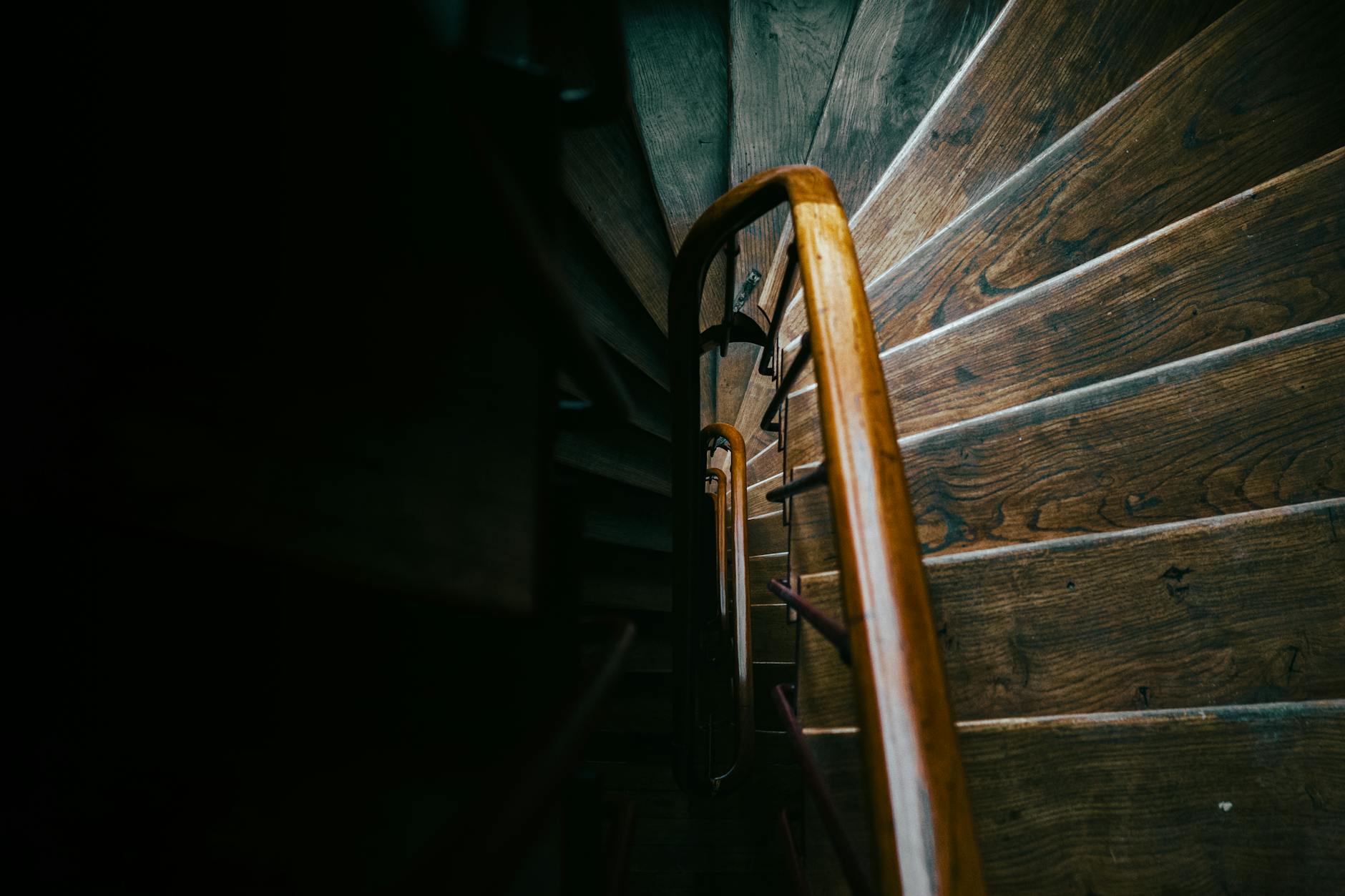 Artistic view of a spiral wooden staircase in Paris, capturing moody shadows and warm lighting.