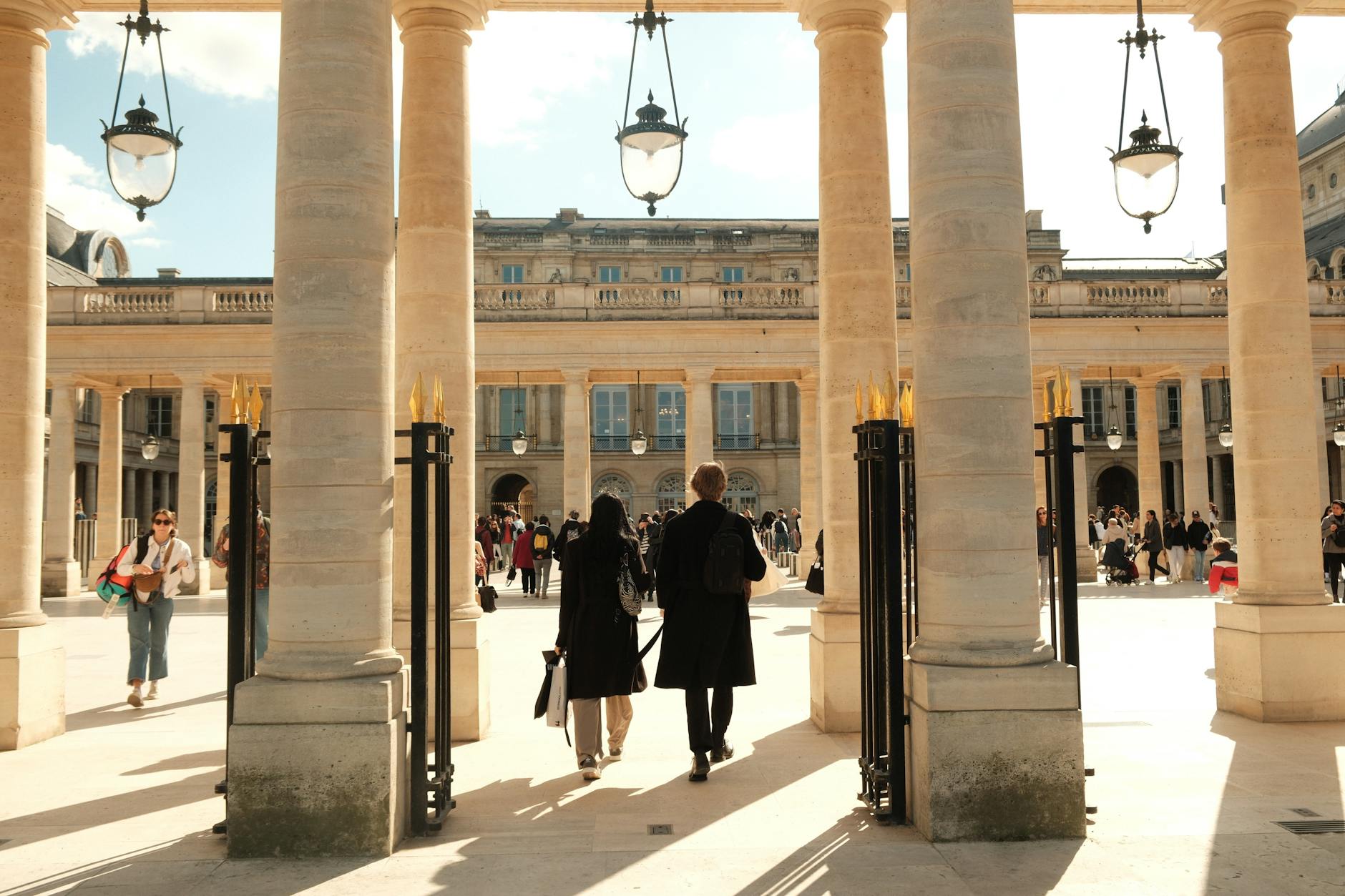 A bustling courtyard in Paris, featuring architectural columns and people enjoying the day.