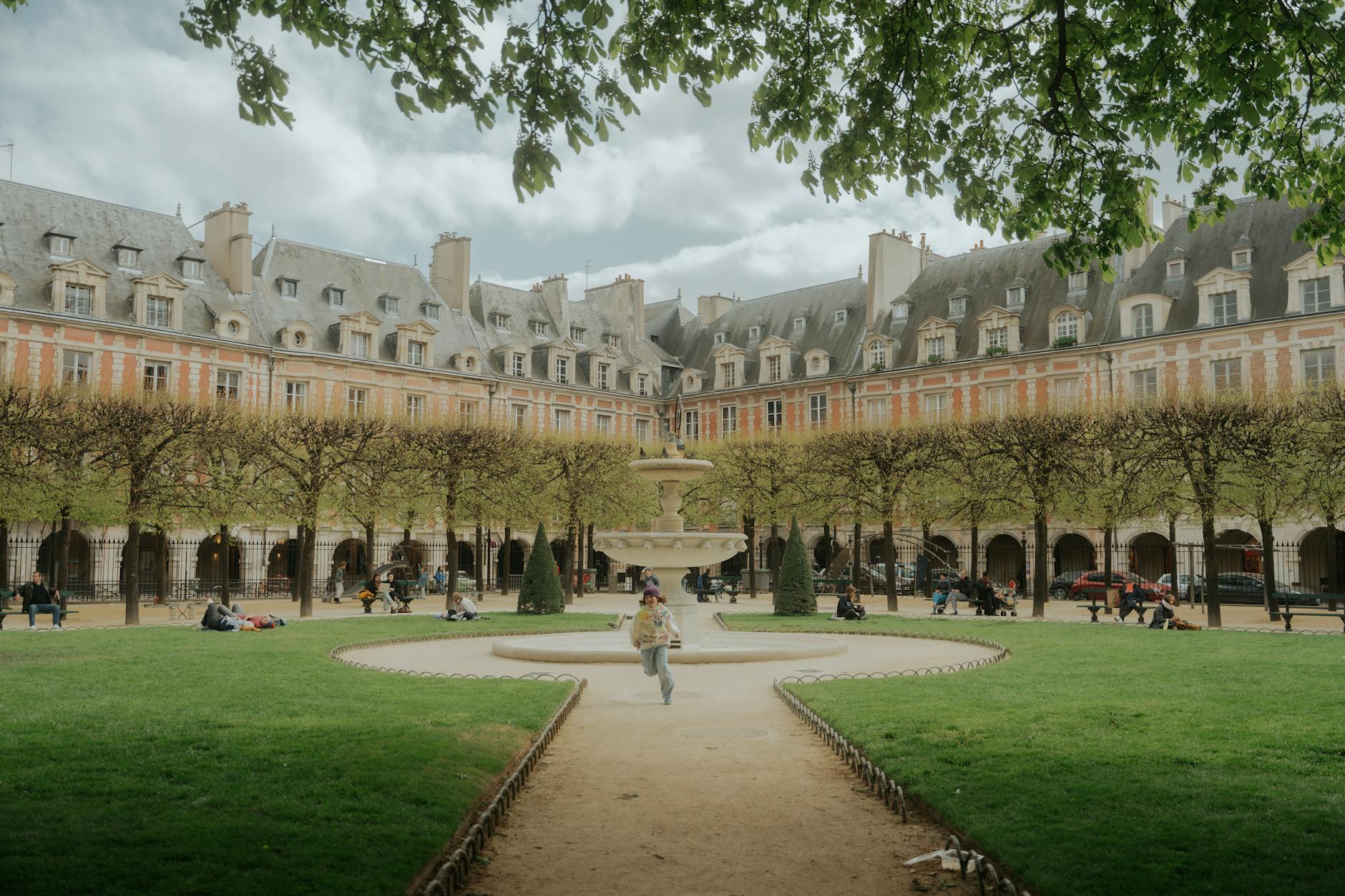 Scenic view of Place des Vosges in Paris with people enjoying leisure time under lush greenery.