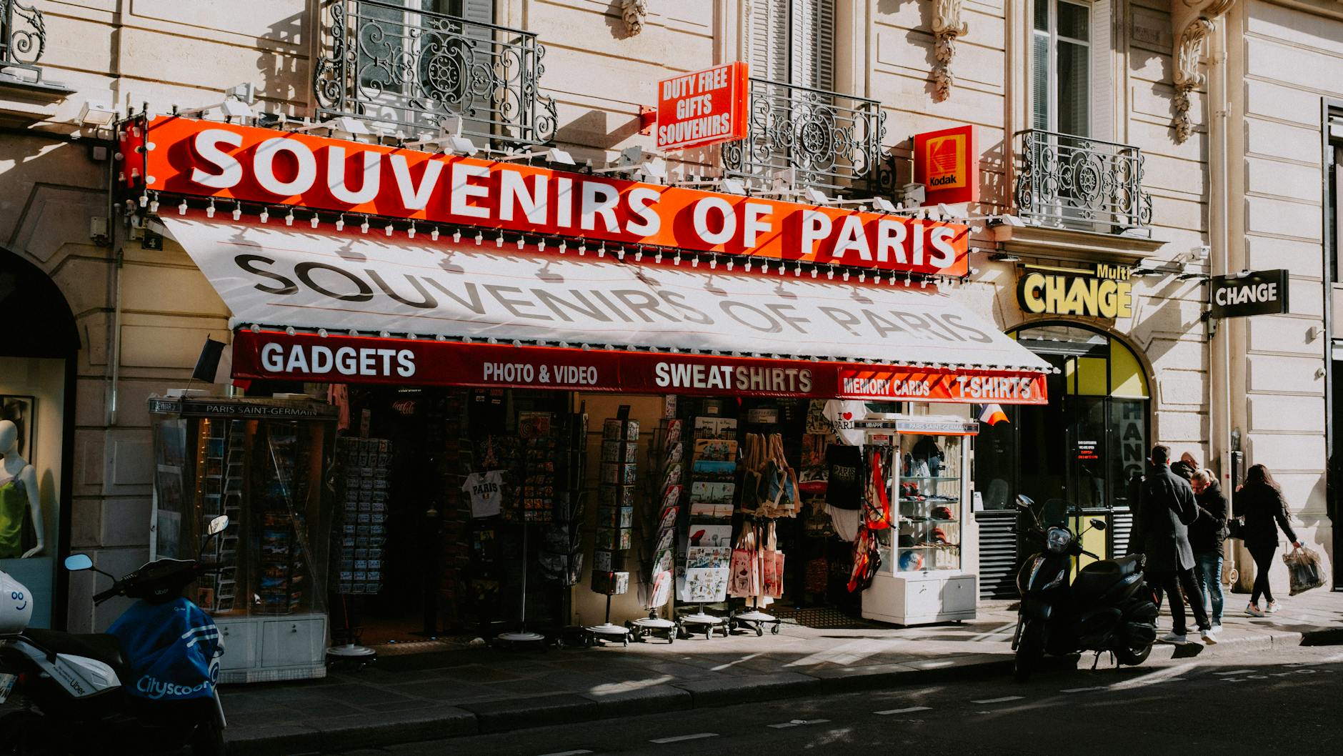 Street view of a Paris souvenir shop with motorbikes, showcasing signage and storefront items.