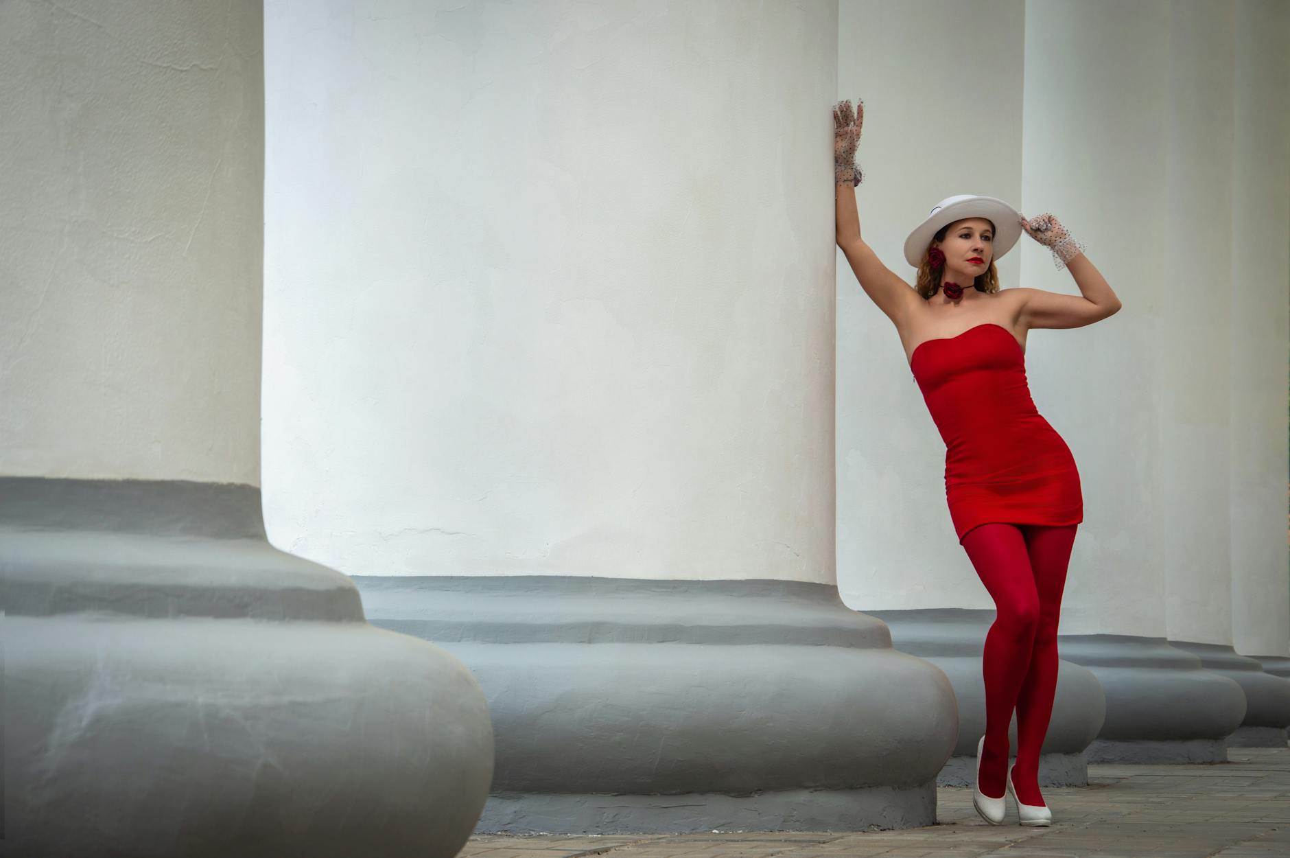 Stylish woman in red posing gracefully beside large classical columns.