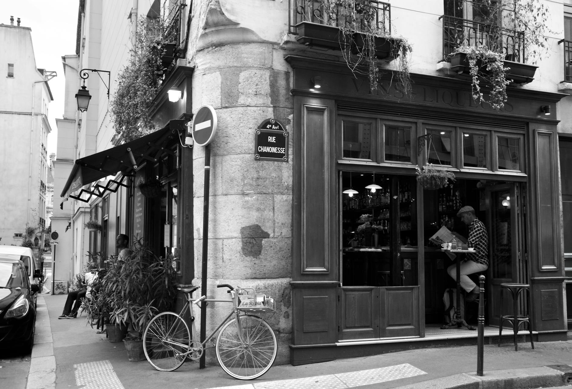 Black and white photo of a quaint Paris street corner featuring a café and a bicycle.