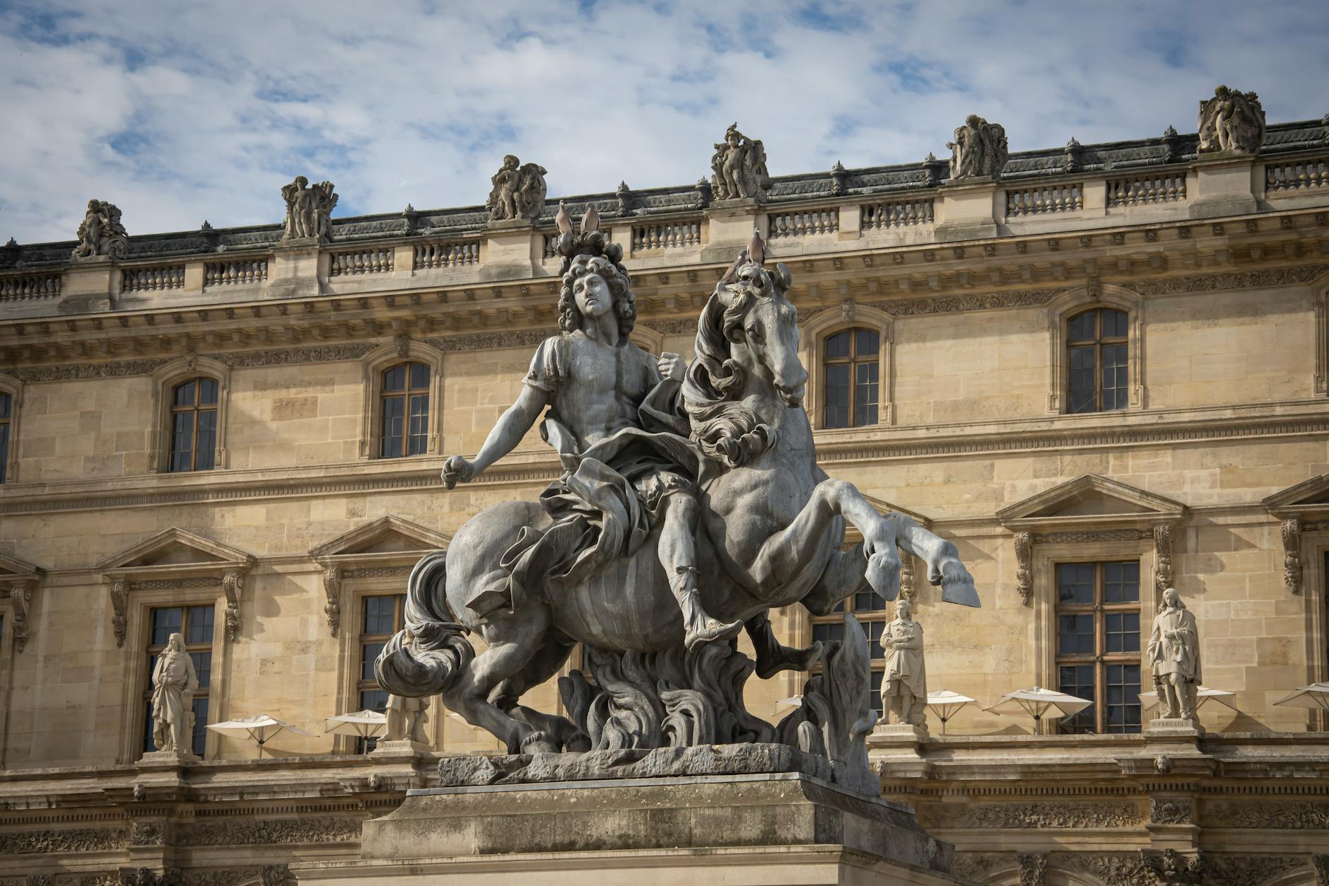 Equestrian statue of Louis XIV in front of the Louvre Museum in Paris, displaying classical French sculpture.