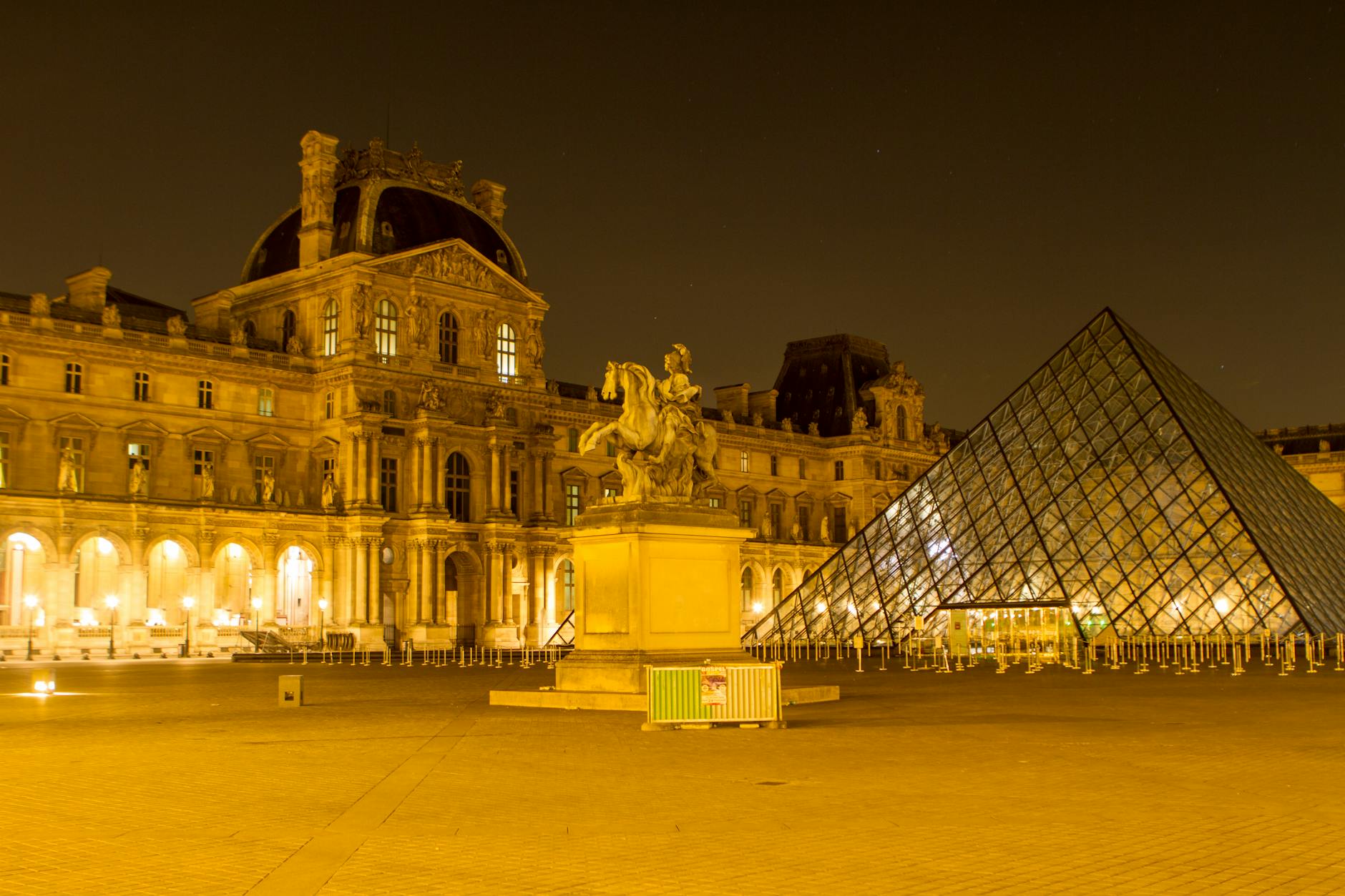 Illuminated view of the Louvre Museum in Paris featuring the iconic glass pyramid and statue at night.