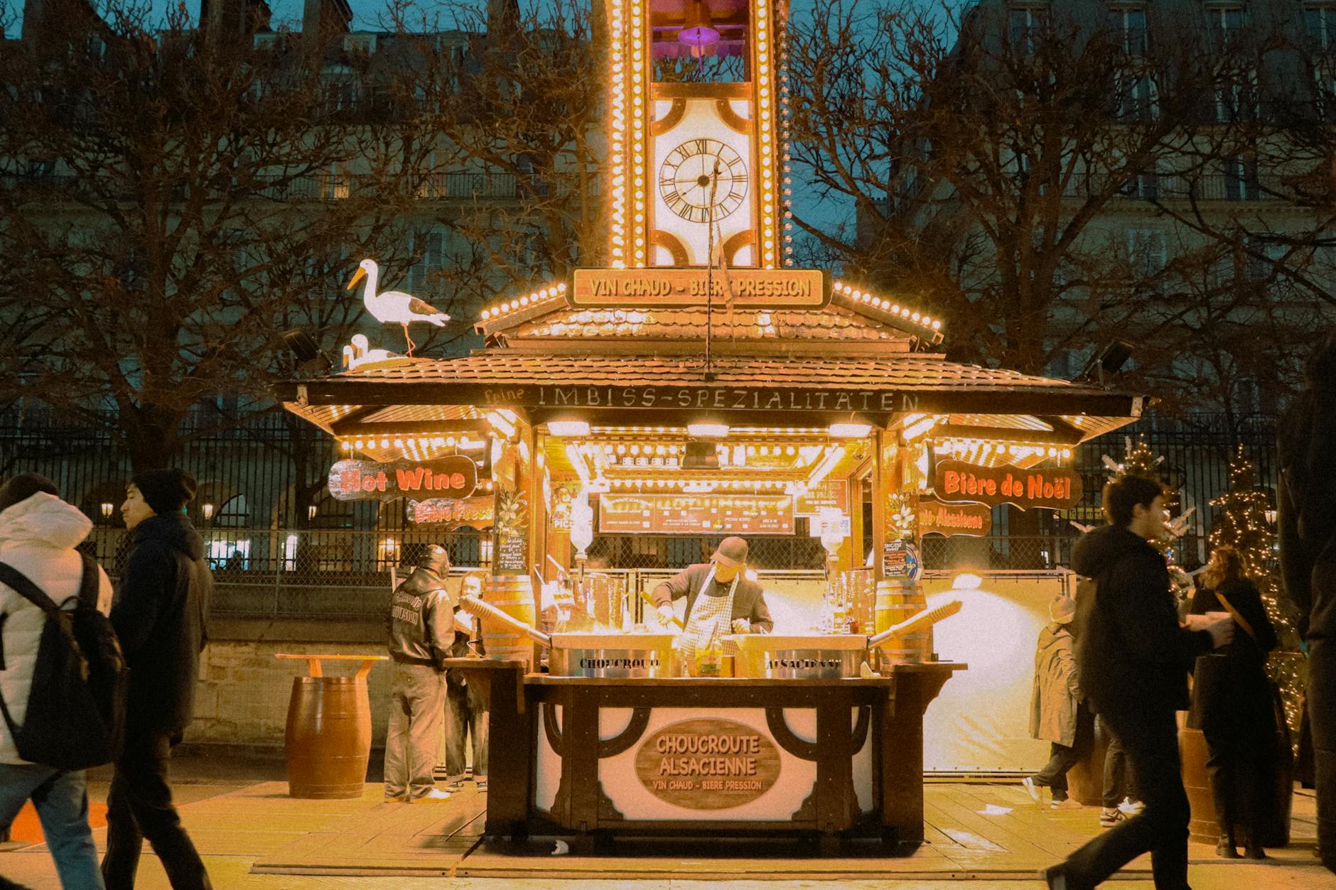 Illuminated Christmas market stall in Paris with people enjoying festive ambiance.