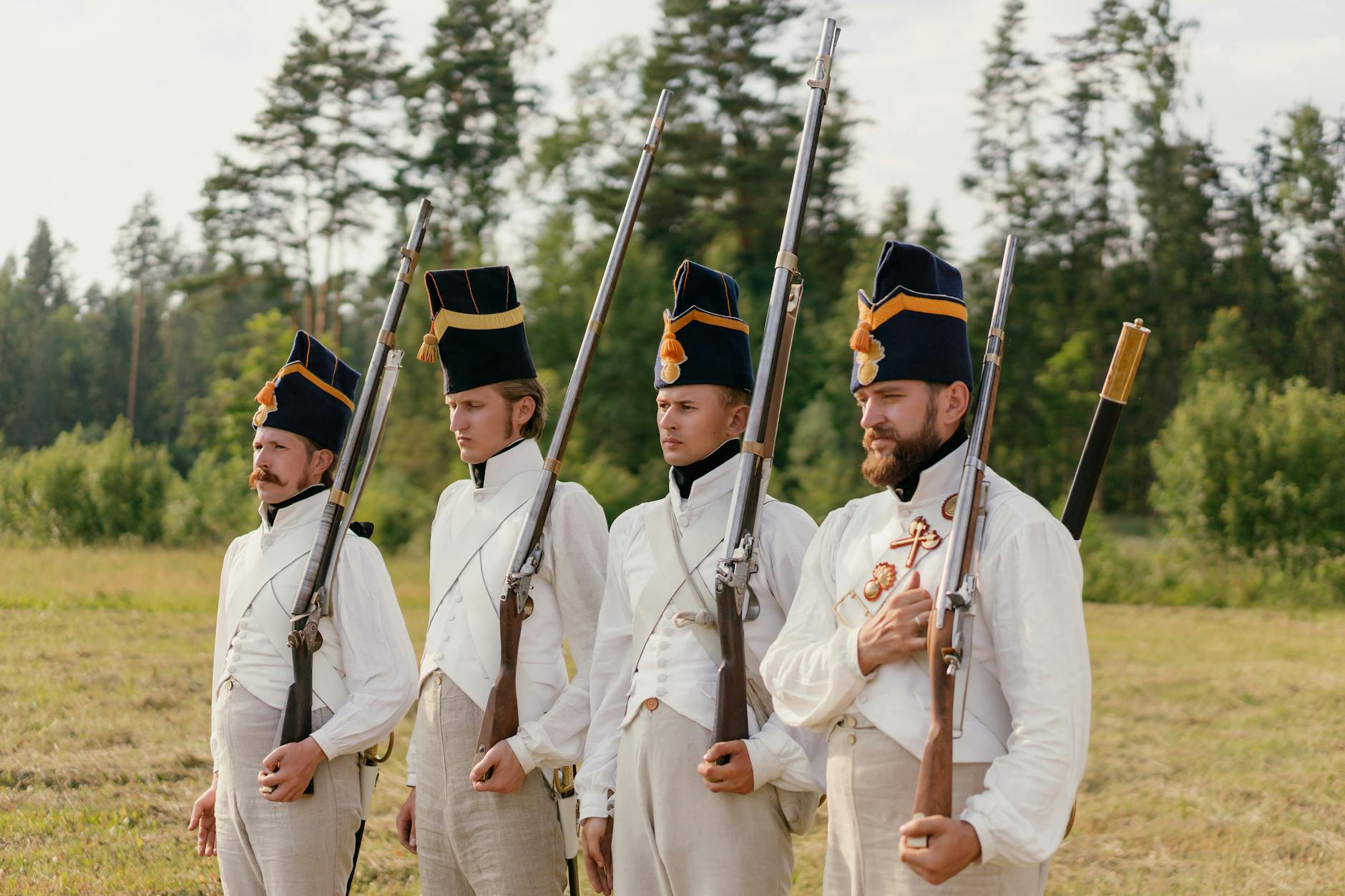 Four soldiers in historical uniforms stand in formation during a reenactment outdoors.