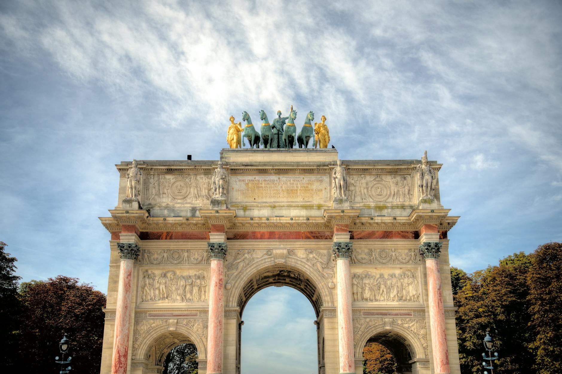 The historic Arc de Triomphe du Carrousel with statues under a bright sky.