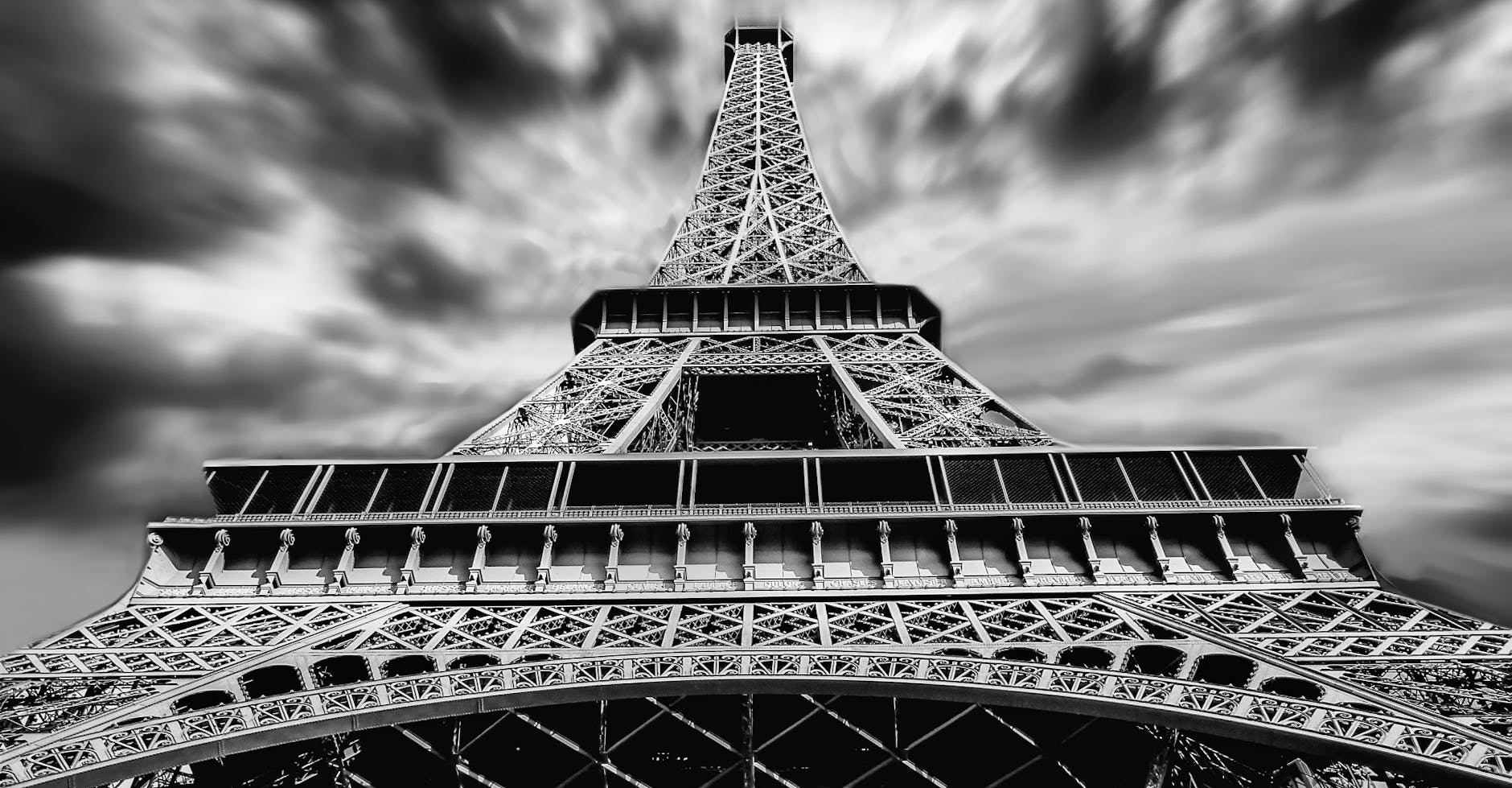 A striking black and white perspective of the Eiffel Tower under dramatic clouds in Paris.