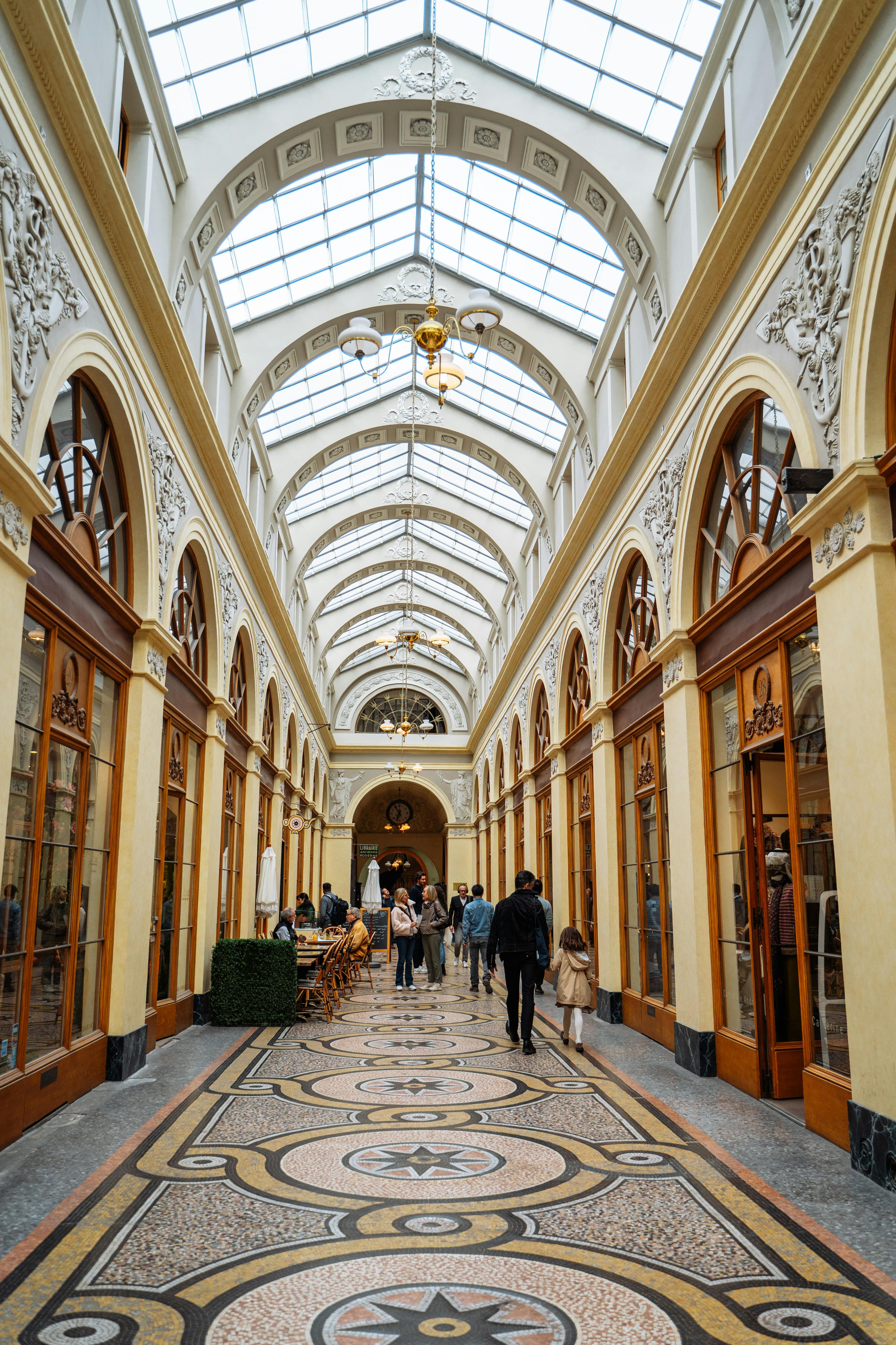 Romantic couple strolling hand-in-hand through a glass-roofed Paris passage on a rainy day