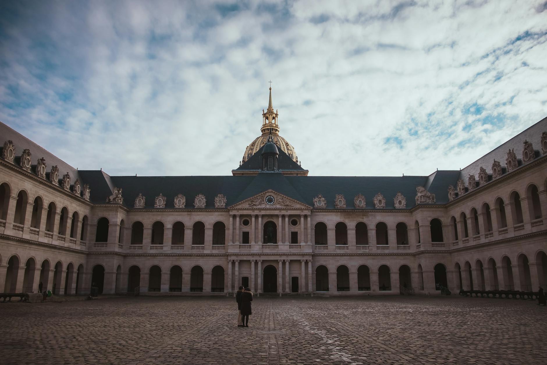 Historic courtyard of Les Invalides with a view of the chapel dome under a cloudy winter sky.