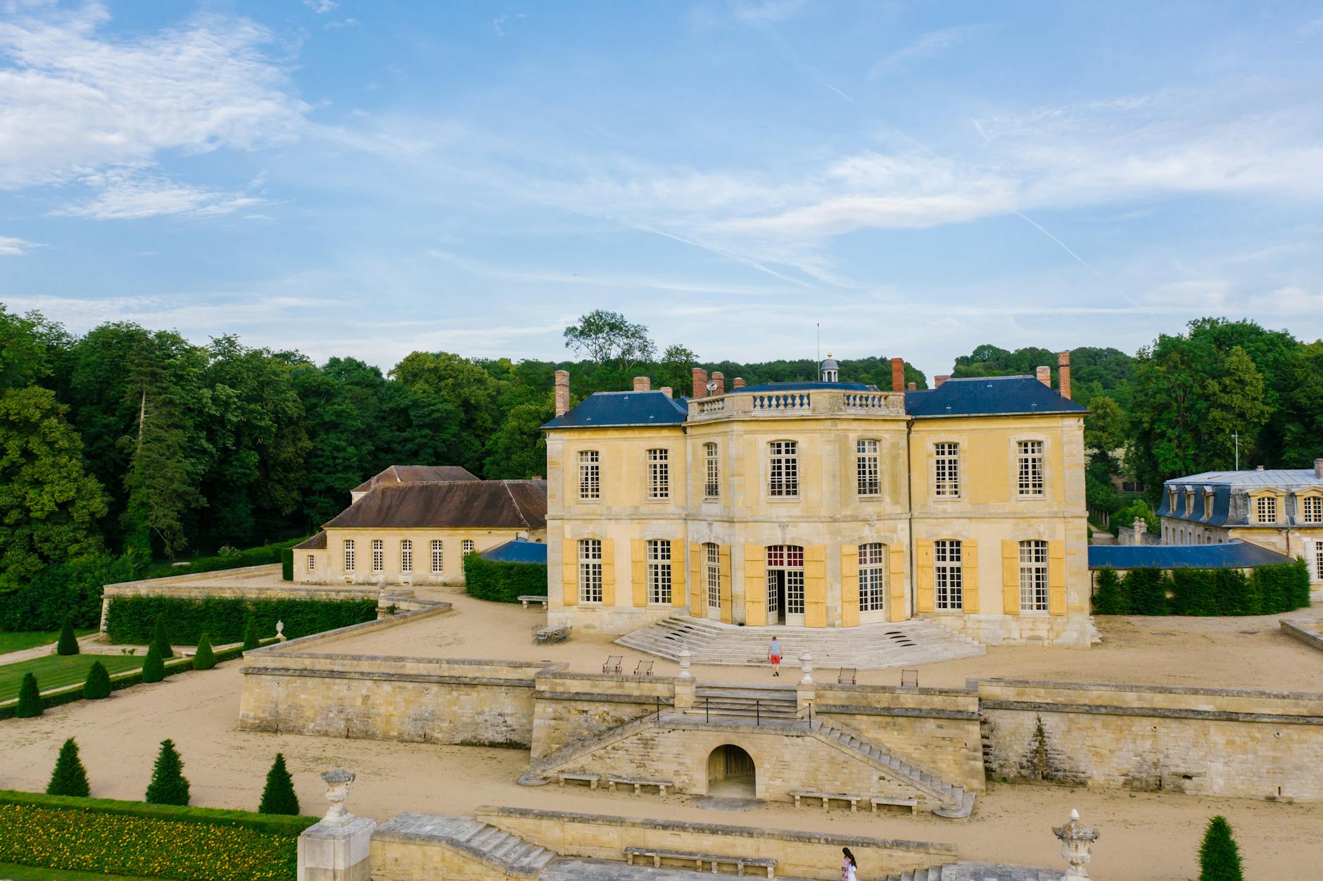 Aerial view of a historic French chateau surrounded by lush gardens and blue sky.