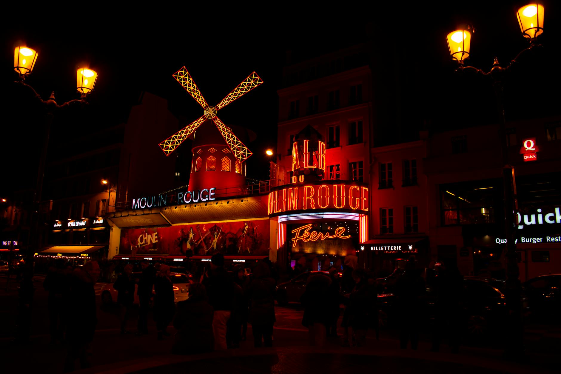 Illuminated night scene of the iconic Moulin Rouge in Paris, featuring its famous red windmill.