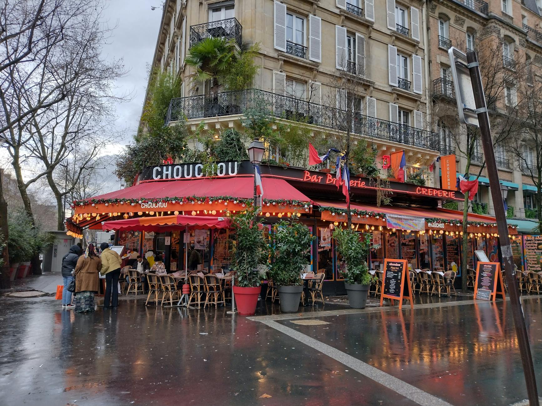 A vibrant Parisian café with outdoor seating, decorated for winter with glowing lights.