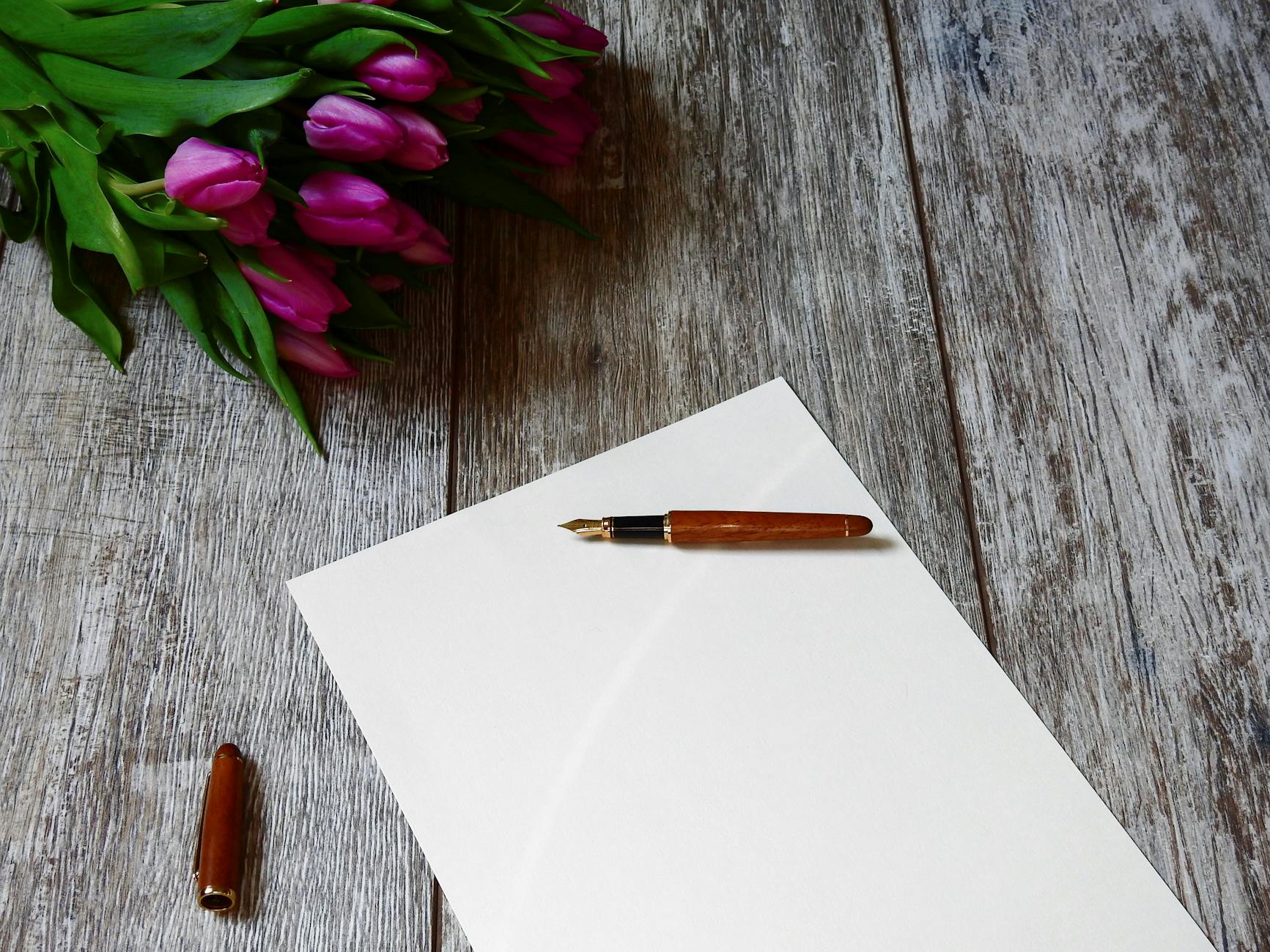 A blank note with a fountain pen and purple tulips on a wooden table, ideal for personalized messages.
