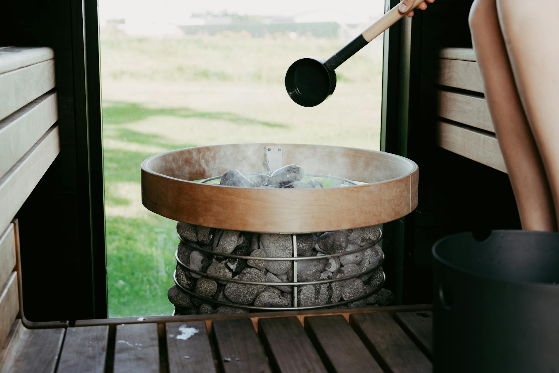 A cozy sauna scene with a person preparing to pour water on hot sauna stones, creating a steamy ambiance.