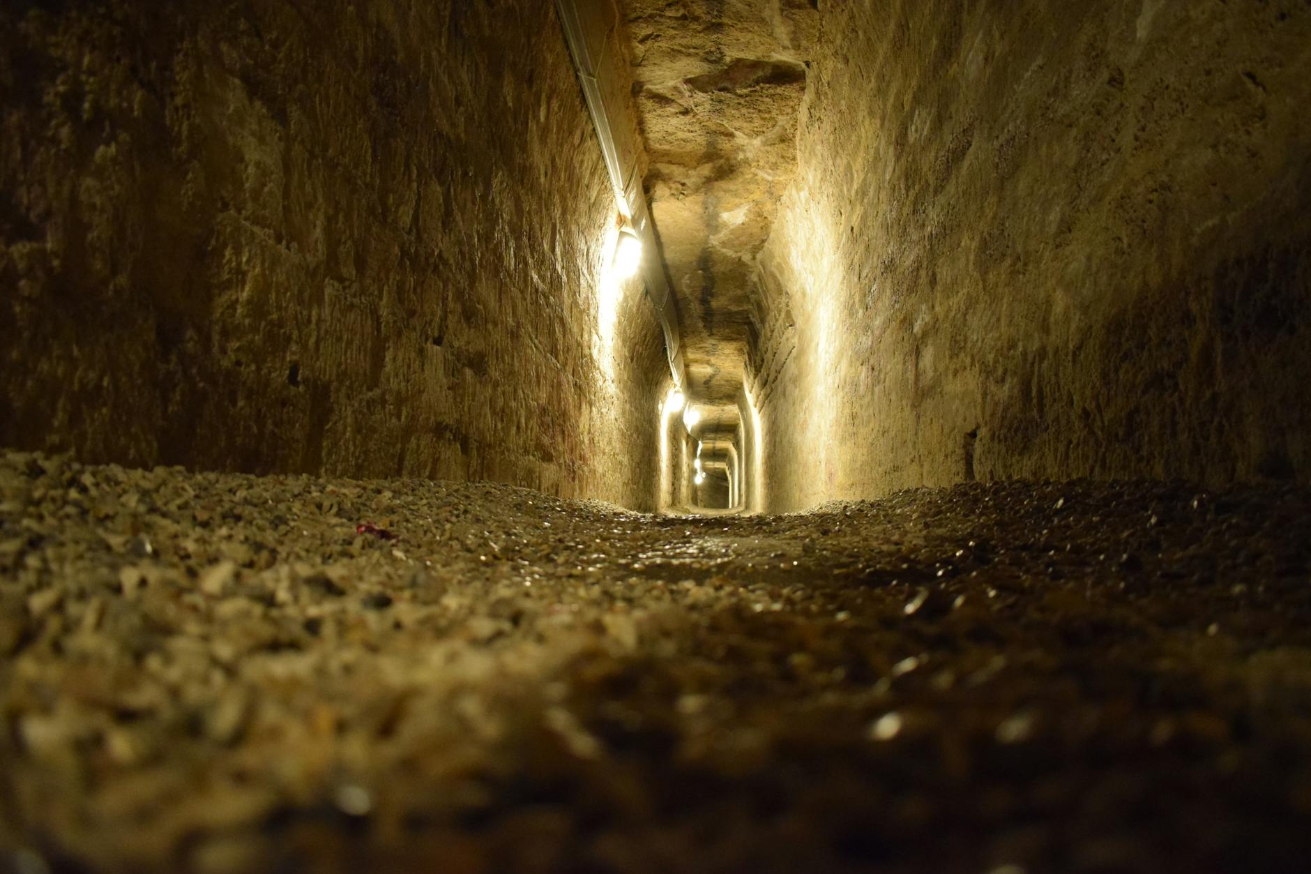 Underground limestone tunnel in Paris catacombs with skeletal remains visible along stone walls