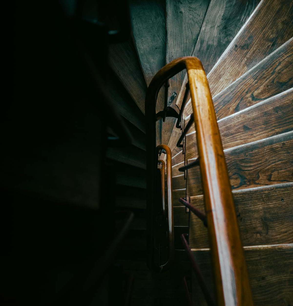 Artistic view of a spiral wooden staircase in Paris, capturing moody shadows and warm lighting.