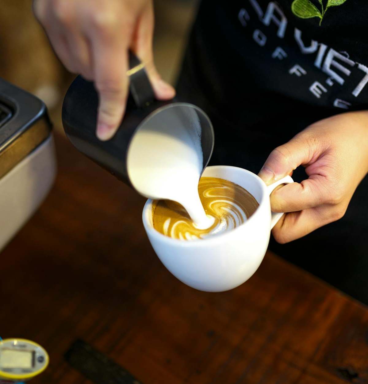 A barista expertly pours milk to create beautiful latte art in a cozy coffee shop setting.