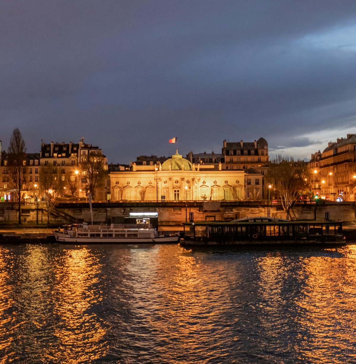 Illuminated Parisian landmarks and bridges reflecting in the Seine at night.