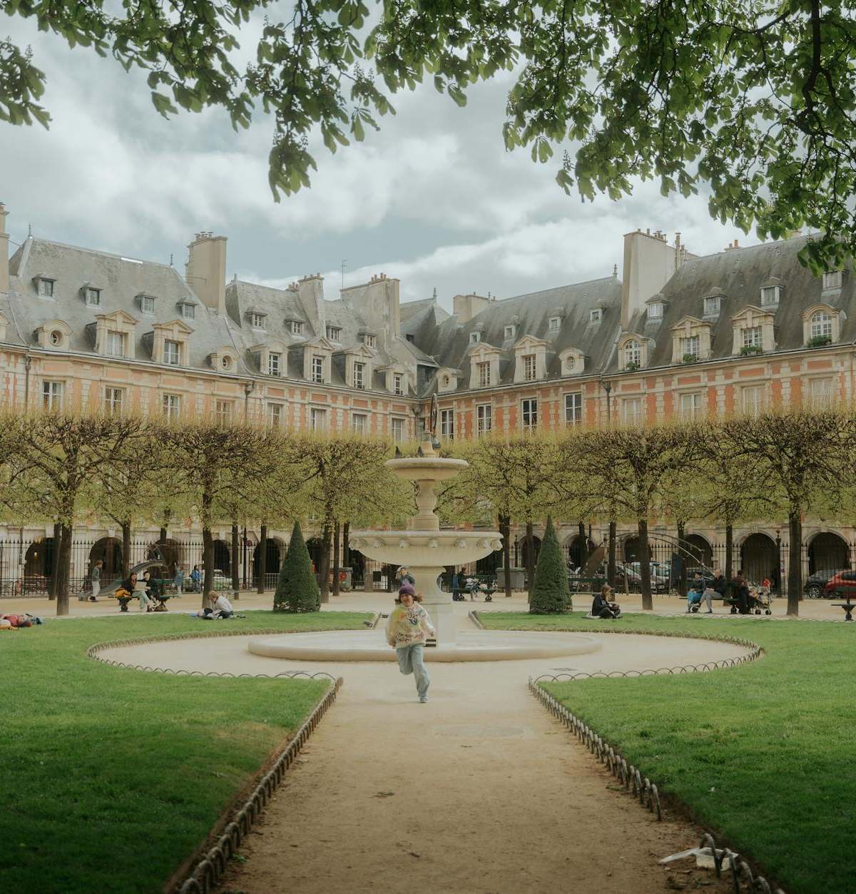 Scenic view of Place des Vosges in Paris with people enjoying leisure time under lush greenery.