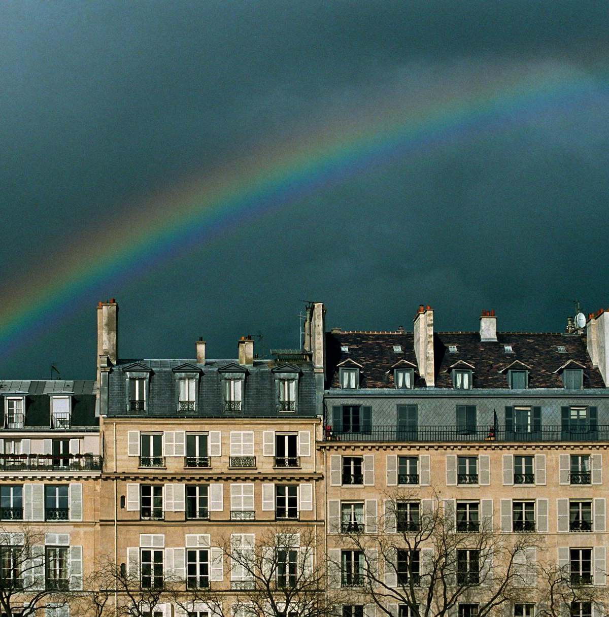 Parisian buildings with a beautiful rainbow arched overhead against a dramatic sky, capturing the city's charm.