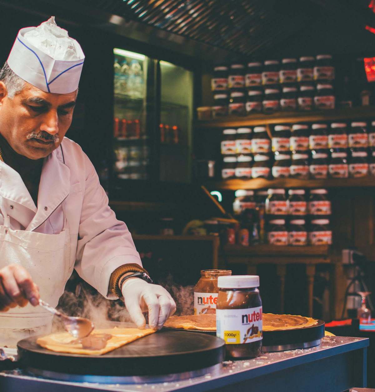 A chef skillfully prepares a Nutella crepe in a cozy Parisian café. Indoor ambiance and culinary expertise.