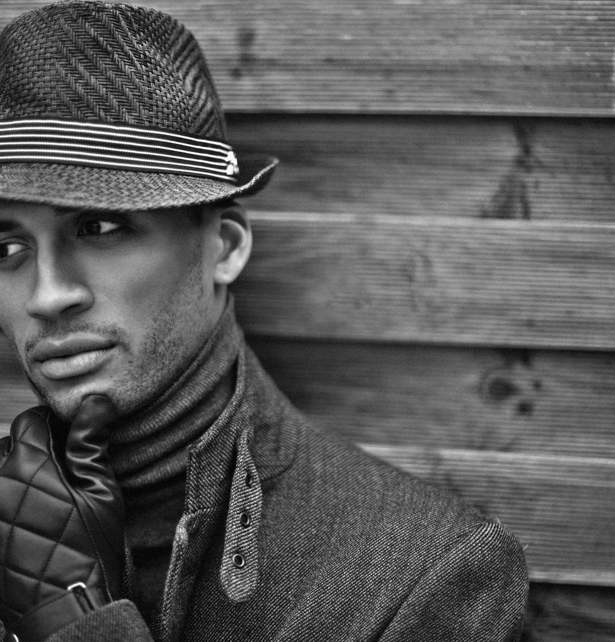 Black and white portrait of a man in a fedora hat, against wooden background in Paris.