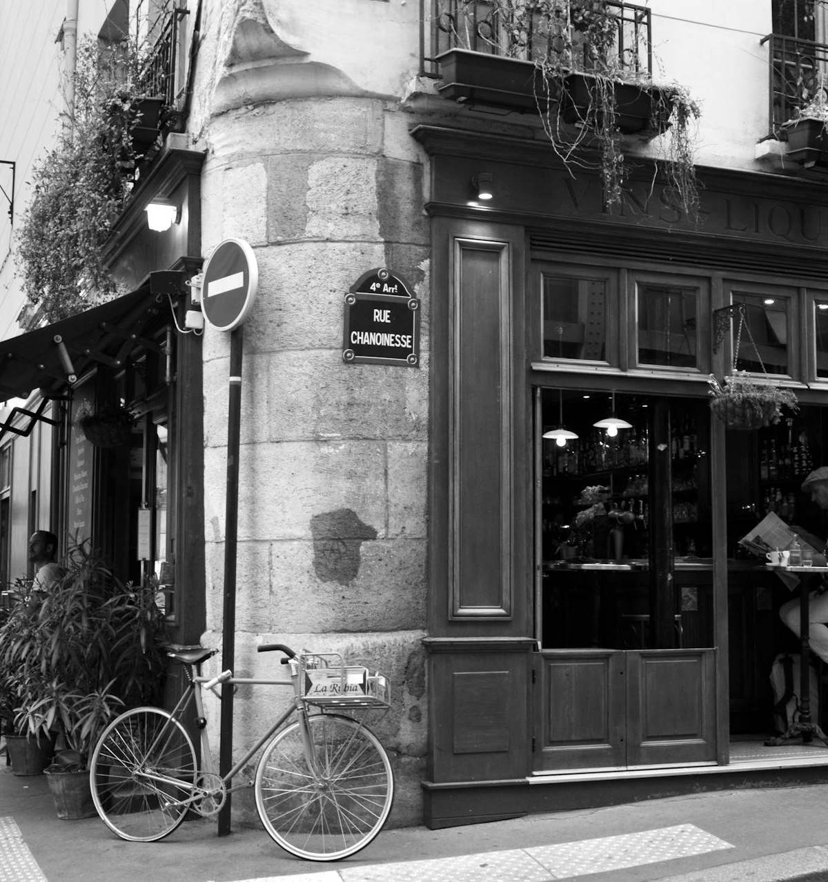 Black and white photo of a quaint Paris street corner featuring a café and a bicycle.