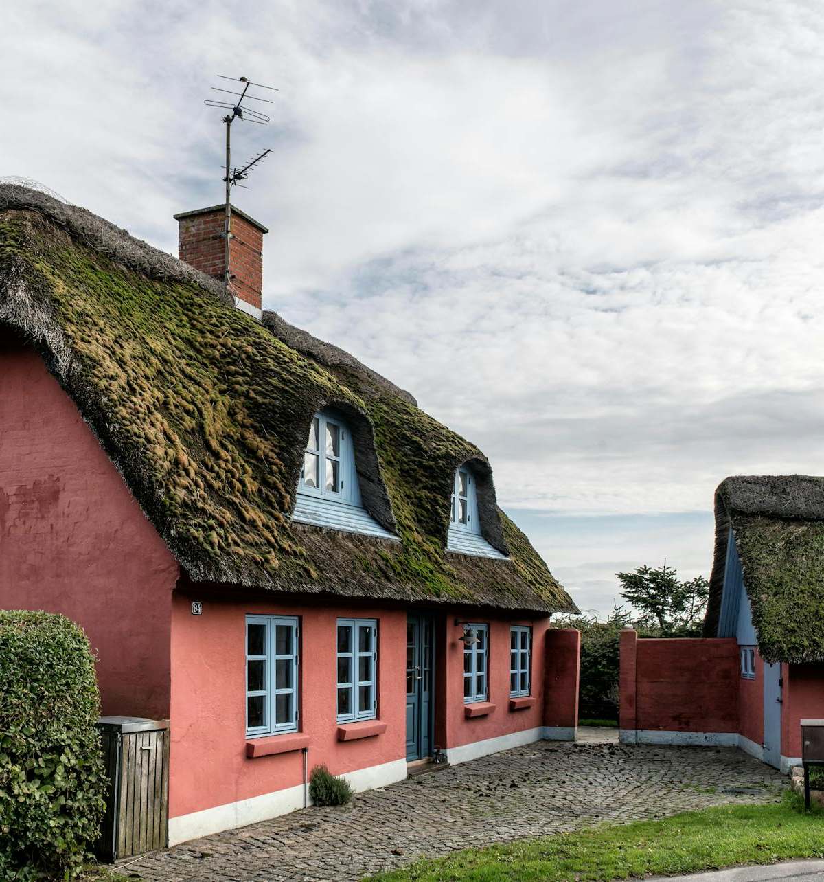 Charming thatched cottages with red walls in Haderslev, Denmark under a cloudy sky.
