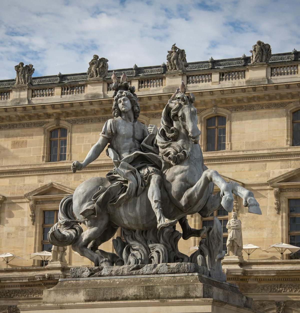 Equestrian statue of Louis XIV in front of the Louvre Museum in Paris, displaying classical French sculpture.