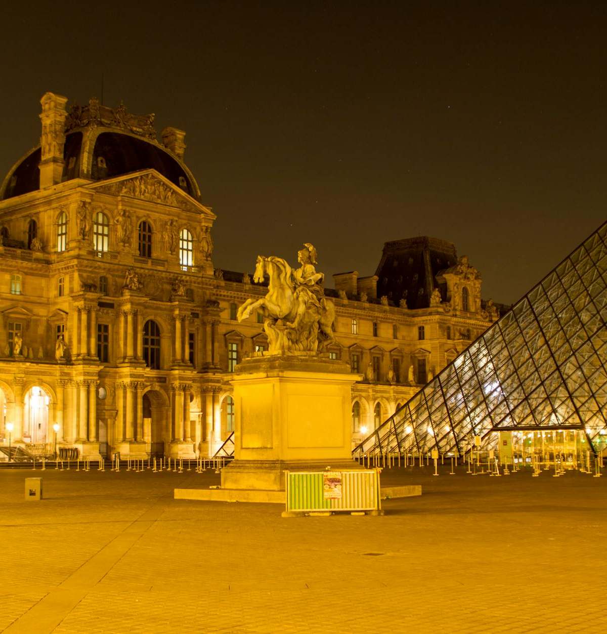 Illuminated view of the Louvre Museum in Paris featuring the iconic glass pyramid and statue at night.