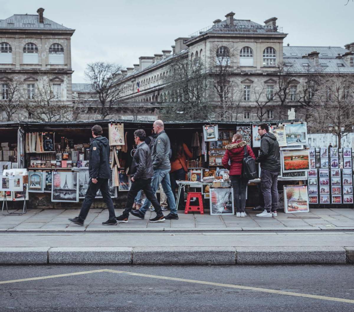 Bustling Paris street with vendors selling art and posters in front of historic buildings.