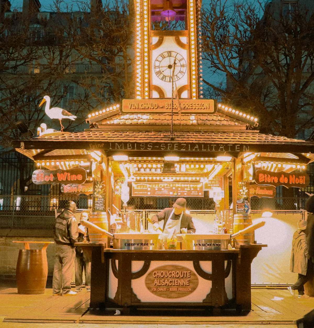 Illuminated Christmas market stall in Paris with people enjoying festive ambiance.
