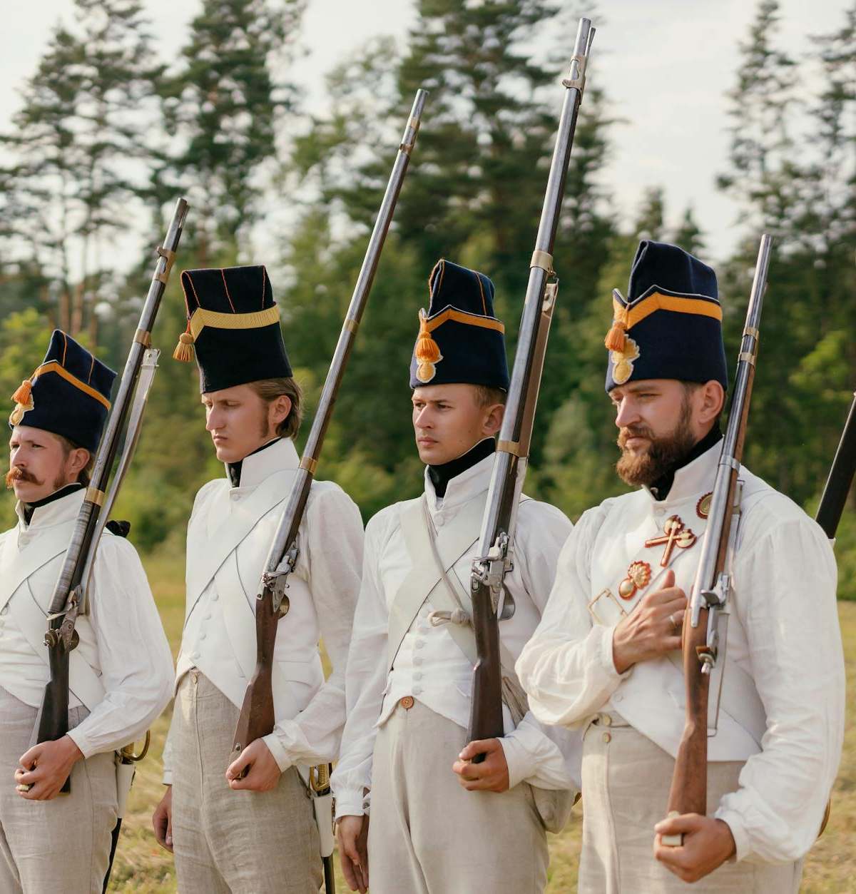 Four soldiers in historical uniforms stand in formation during a reenactment outdoors.