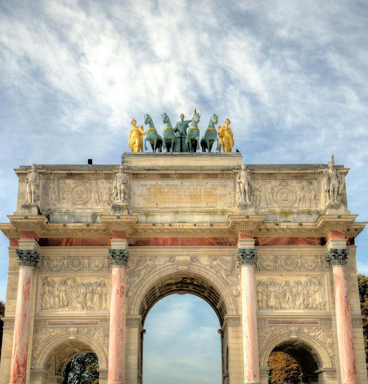 The historic Arc de Triomphe du Carrousel with statues under a bright sky.