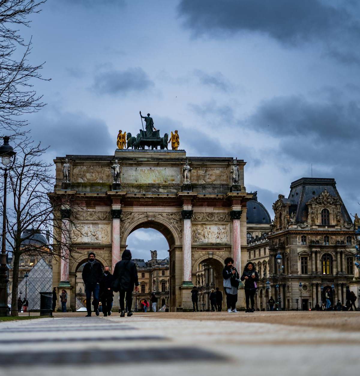 Night view of Arc de Triomphe du Carrousel in Paris with people walking nearby.