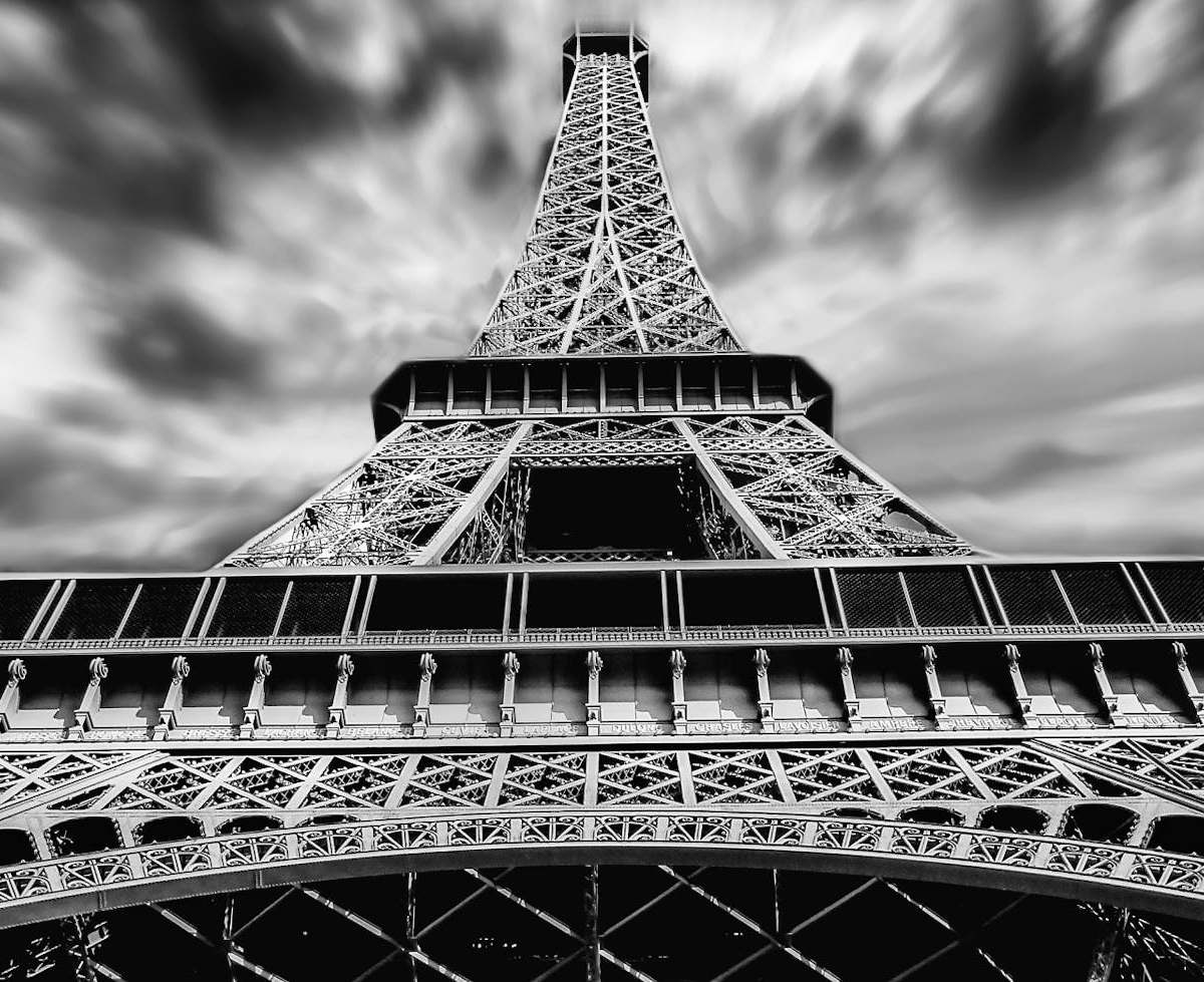 A striking black and white perspective of the Eiffel Tower under dramatic clouds in Paris.