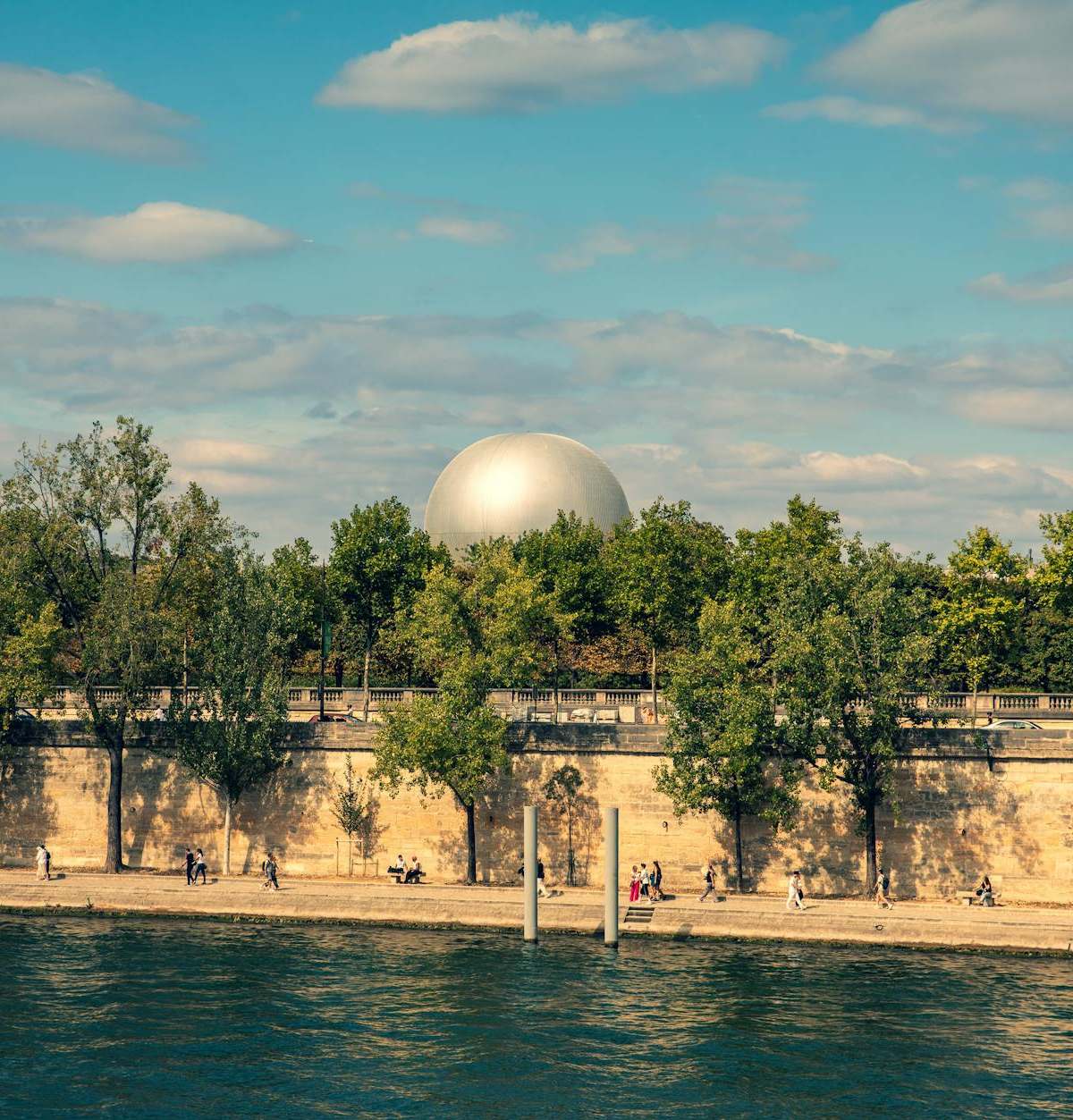 Picturesque view of a sunny Paris riverbank with trees, a Ferris wheel, and dome.