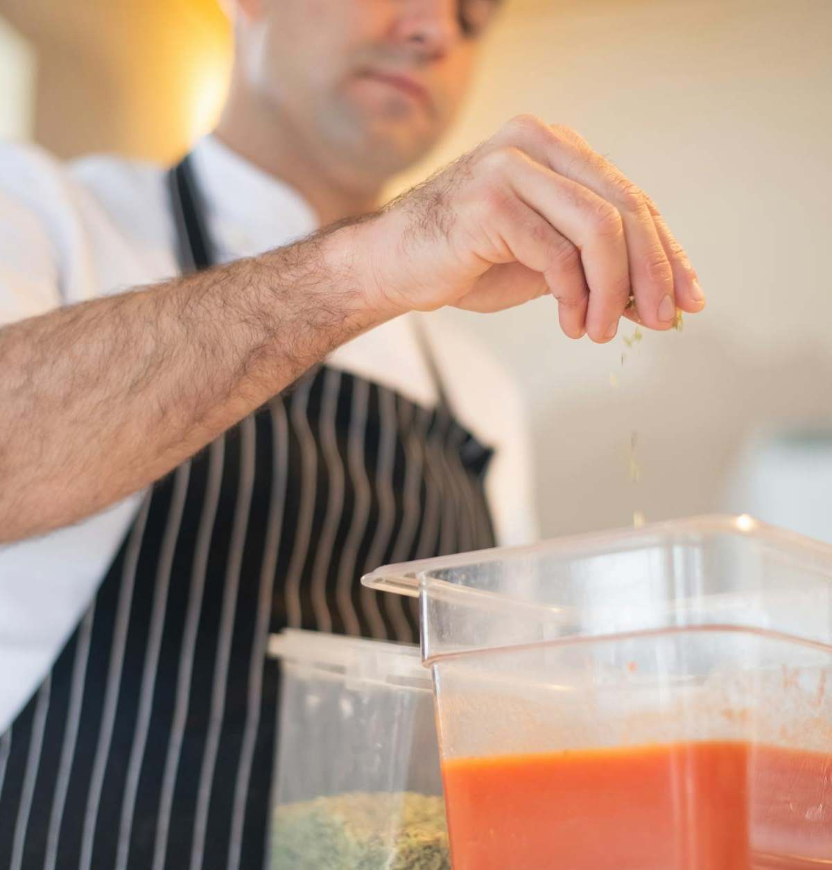 Chef in Portugal skillfully seasons tomato sauce in a modern kitchen setting.