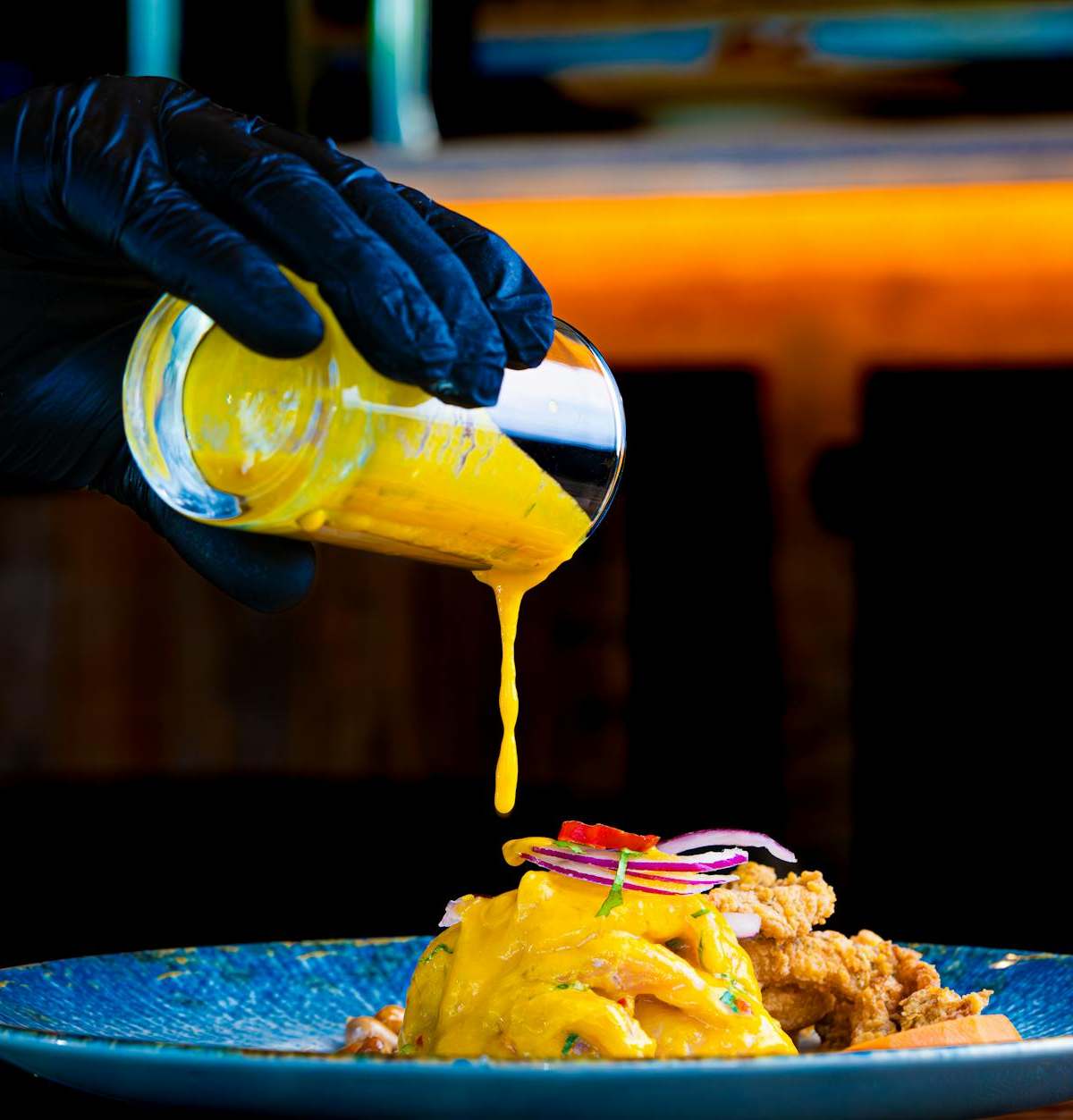 Chef pouring vibrant yellow sauce on gourmet dish. Perfect for culinary and food photography.