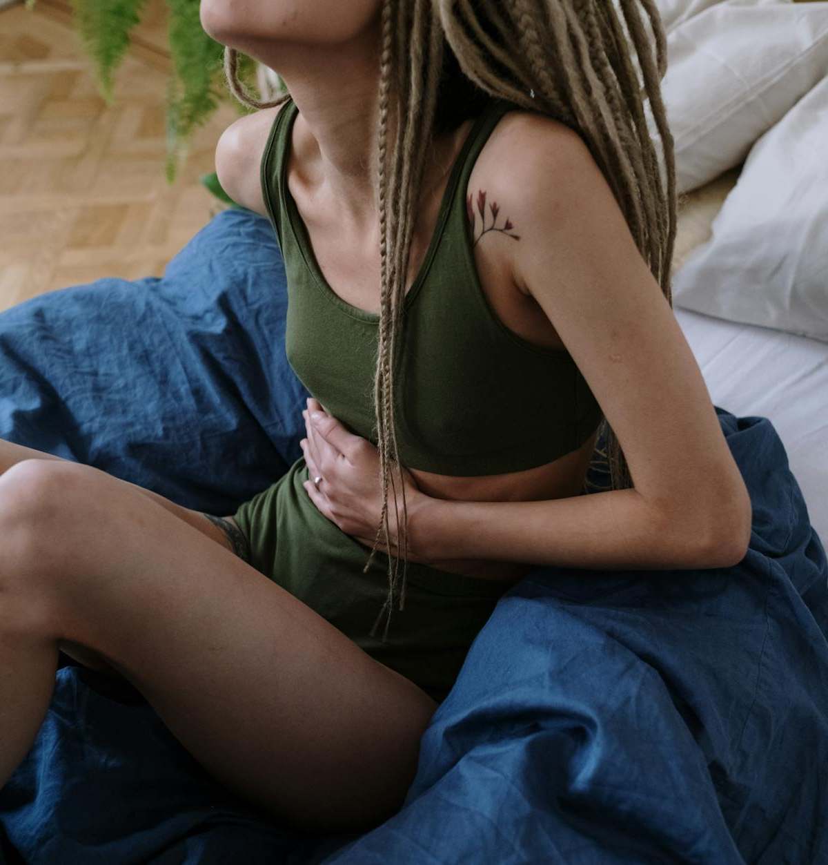 Woman sitting in bed holding her stomach, indicating pain or discomfort, possibly due to cramps.