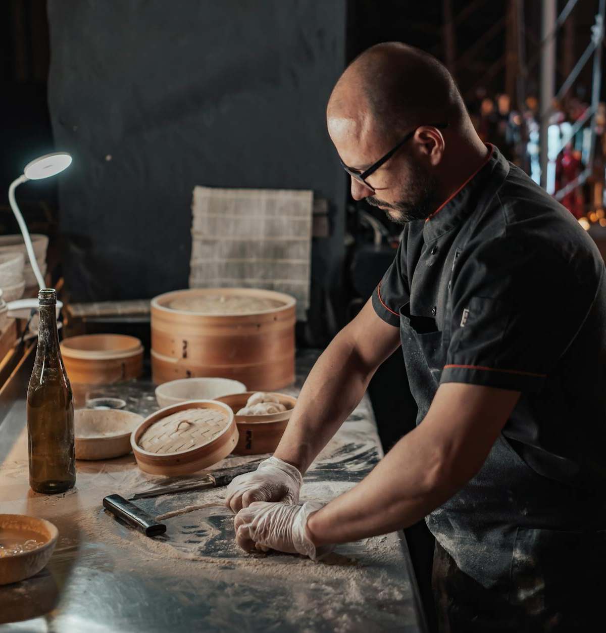 Chef preparing dumplings on a countertop with bamboo steamers in an indoor kitchen setting.