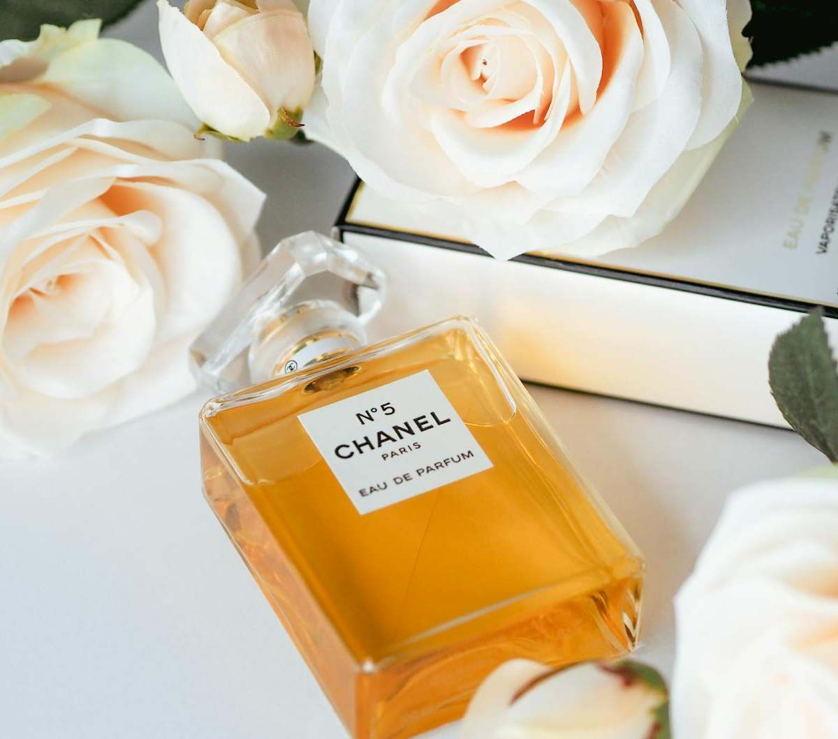 Chanel No. 5 perfume bottle surrounded by elegant white roses showcasing luxury and sophistication.