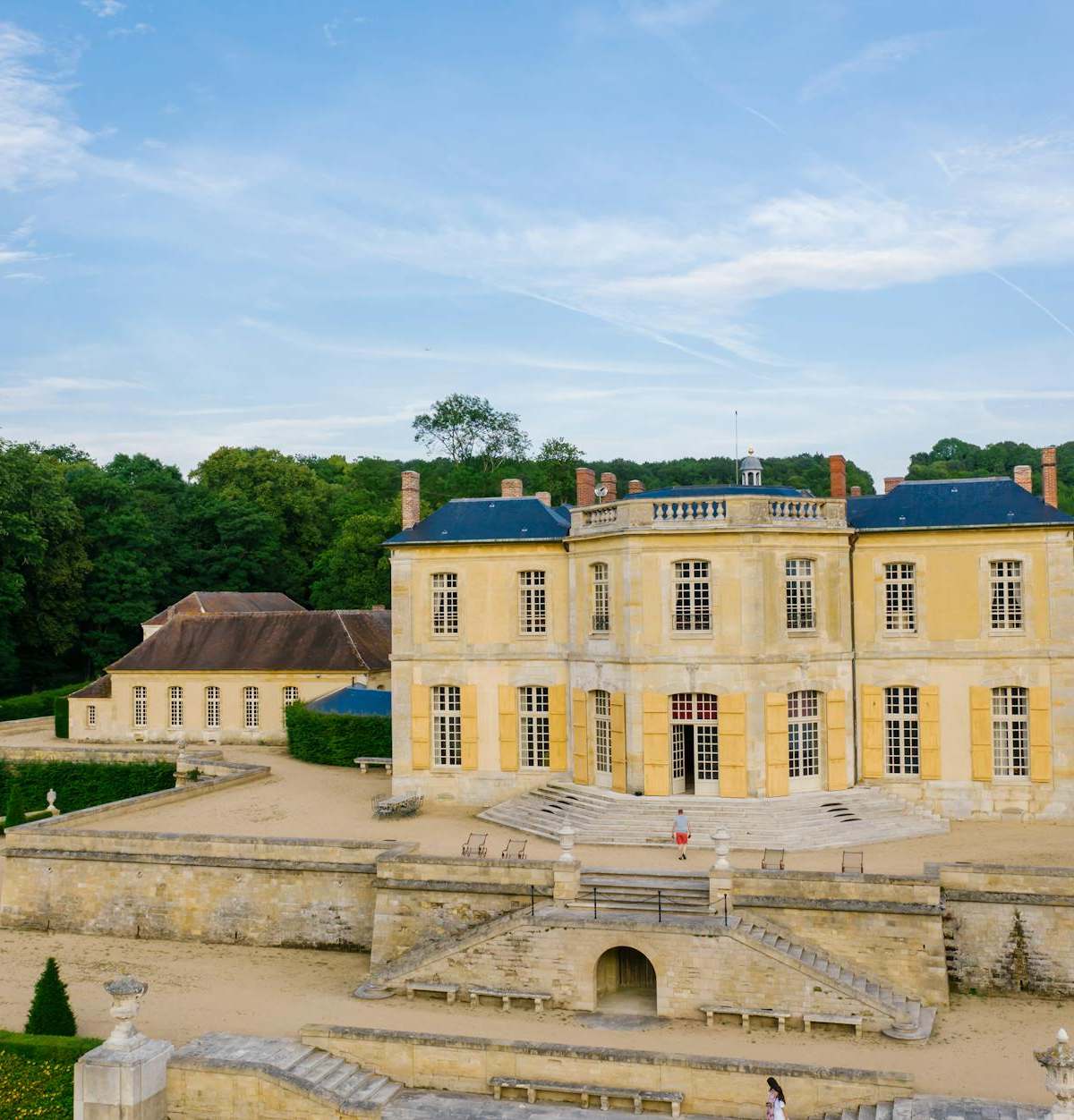 Aerial view of a historic French chateau surrounded by lush gardens and blue sky.