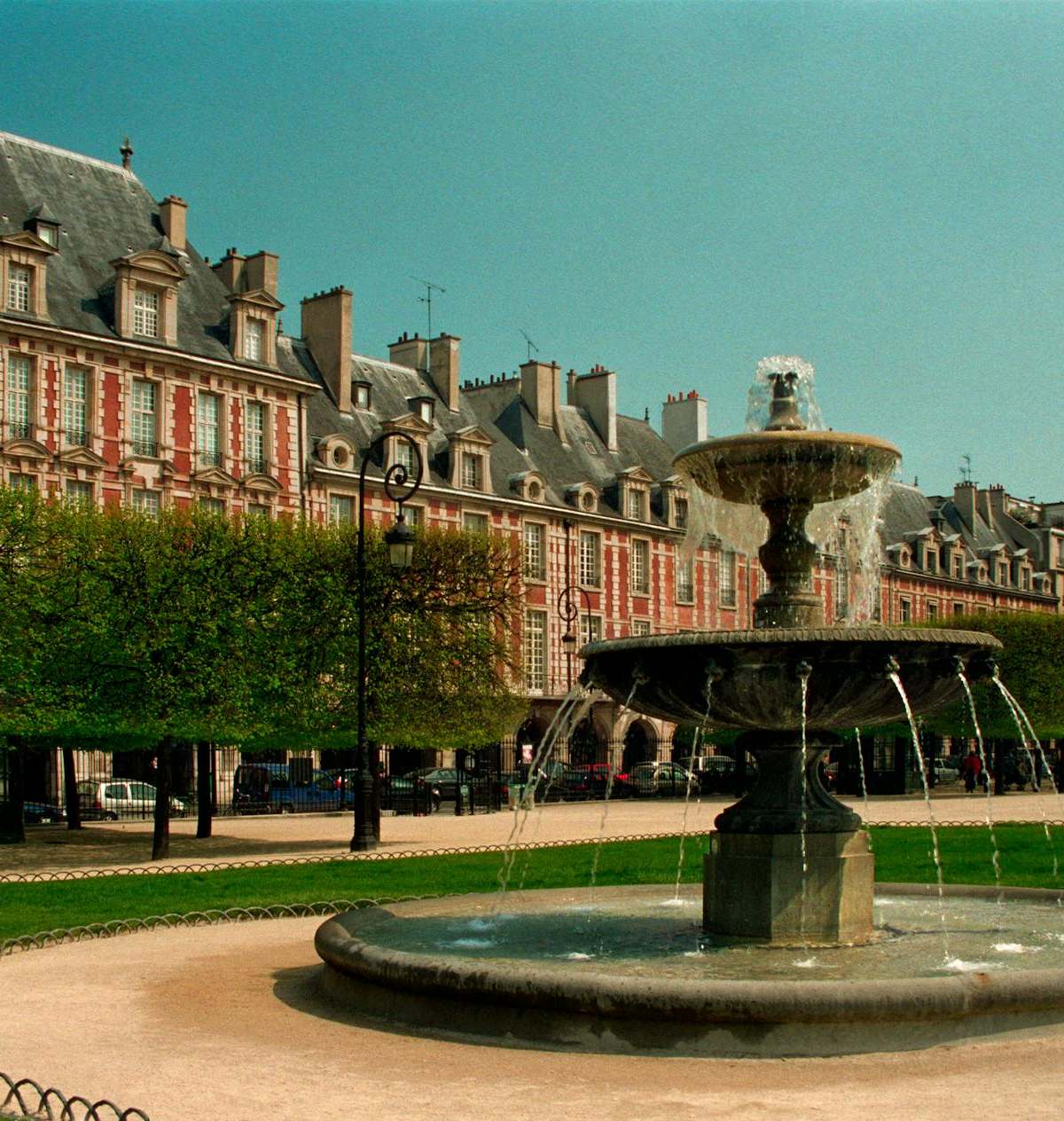 View of the iconic Place des Vosges with fountain in Paris, France, under a clear sky.