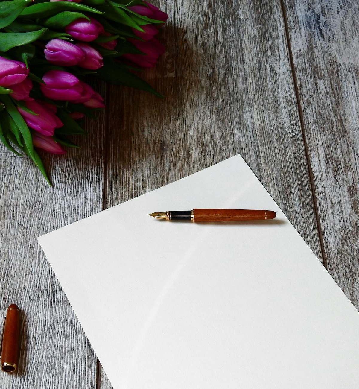 A blank note with a fountain pen and purple tulips on a wooden table, ideal for personalized messages.