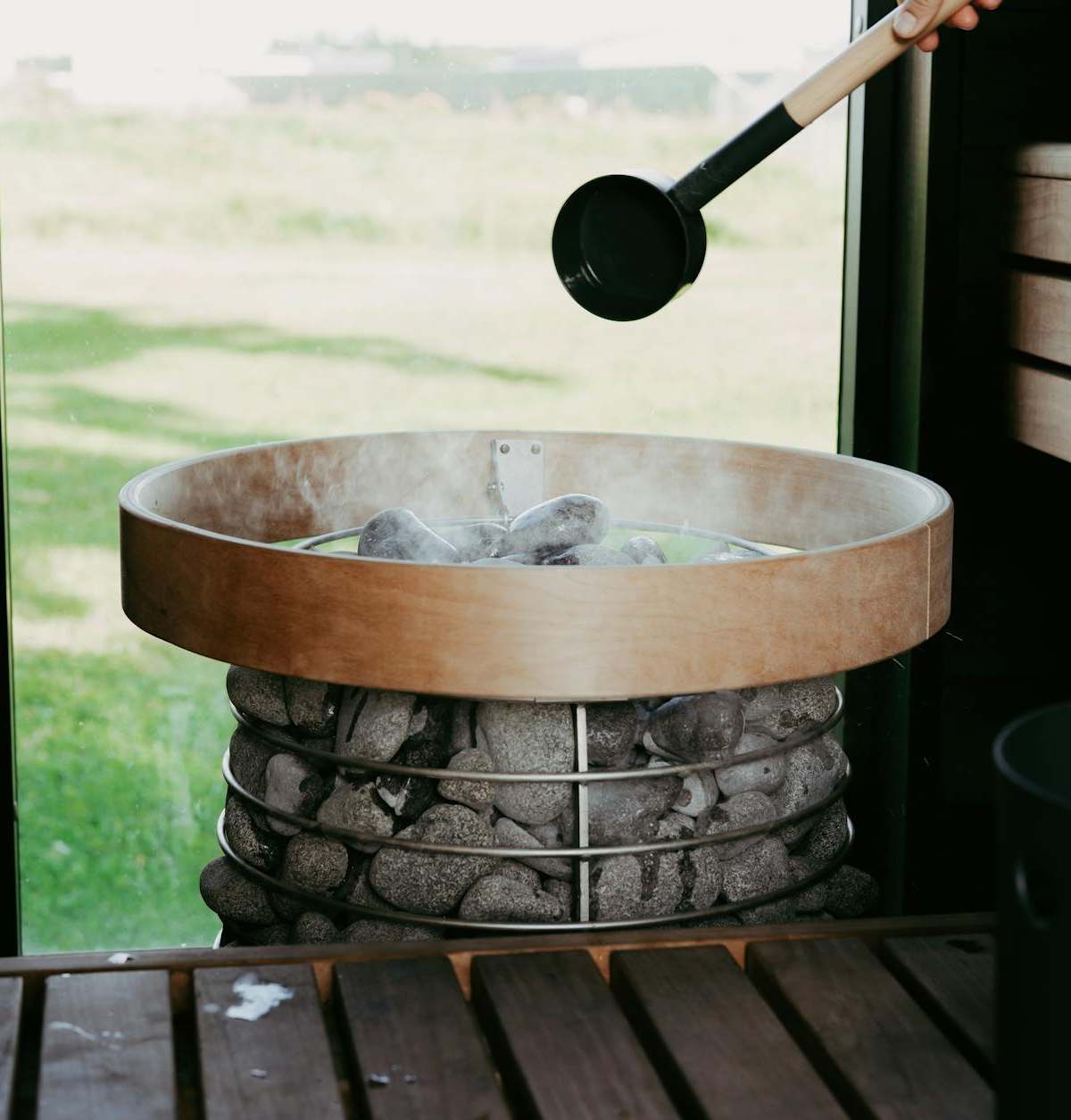 A cozy sauna scene with a person preparing to pour water on hot sauna stones, creating a steamy ambiance.