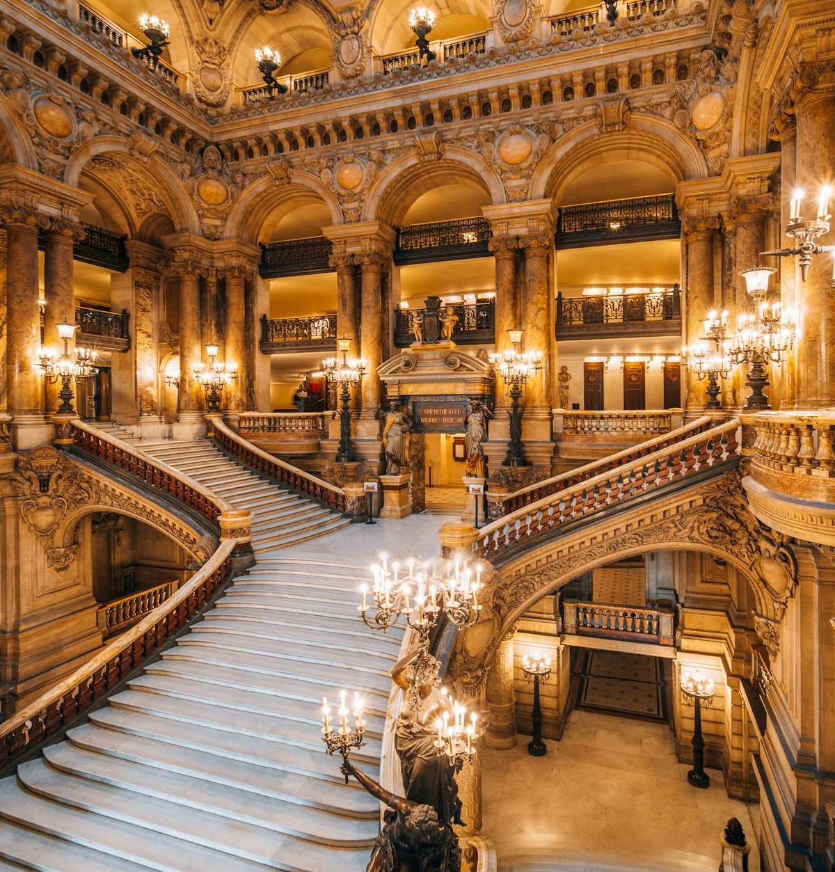 Stunning view of a grand ornate opera house staircase illuminated with chandeliers.