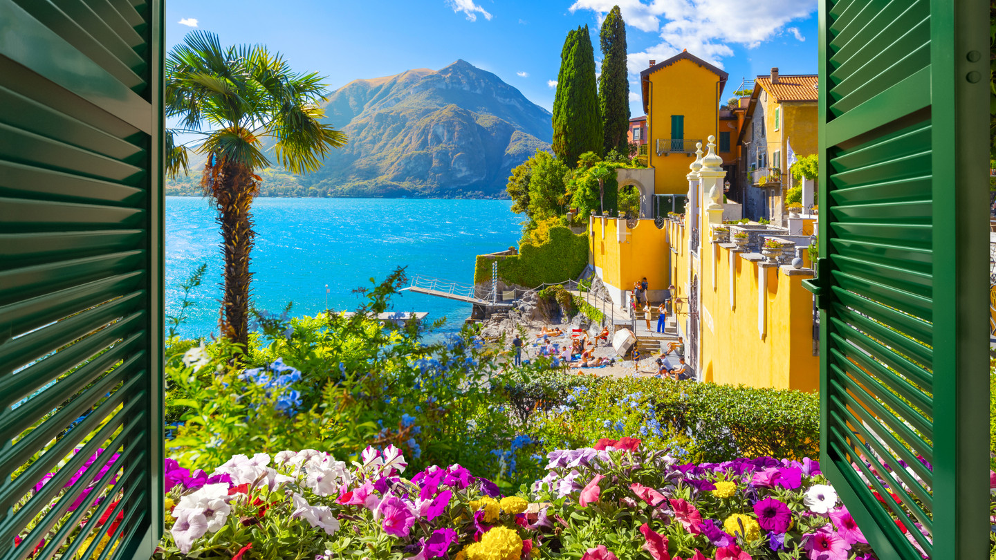Sunny view of Lake Como from a window with beautiful yellow house and flowers, Italian Lakes, Italy